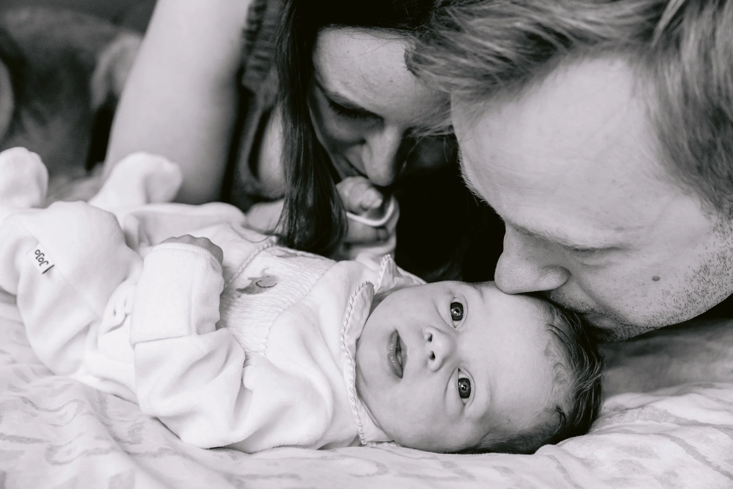 Mum and dad kissing their newborn baby during a photo session in South West London