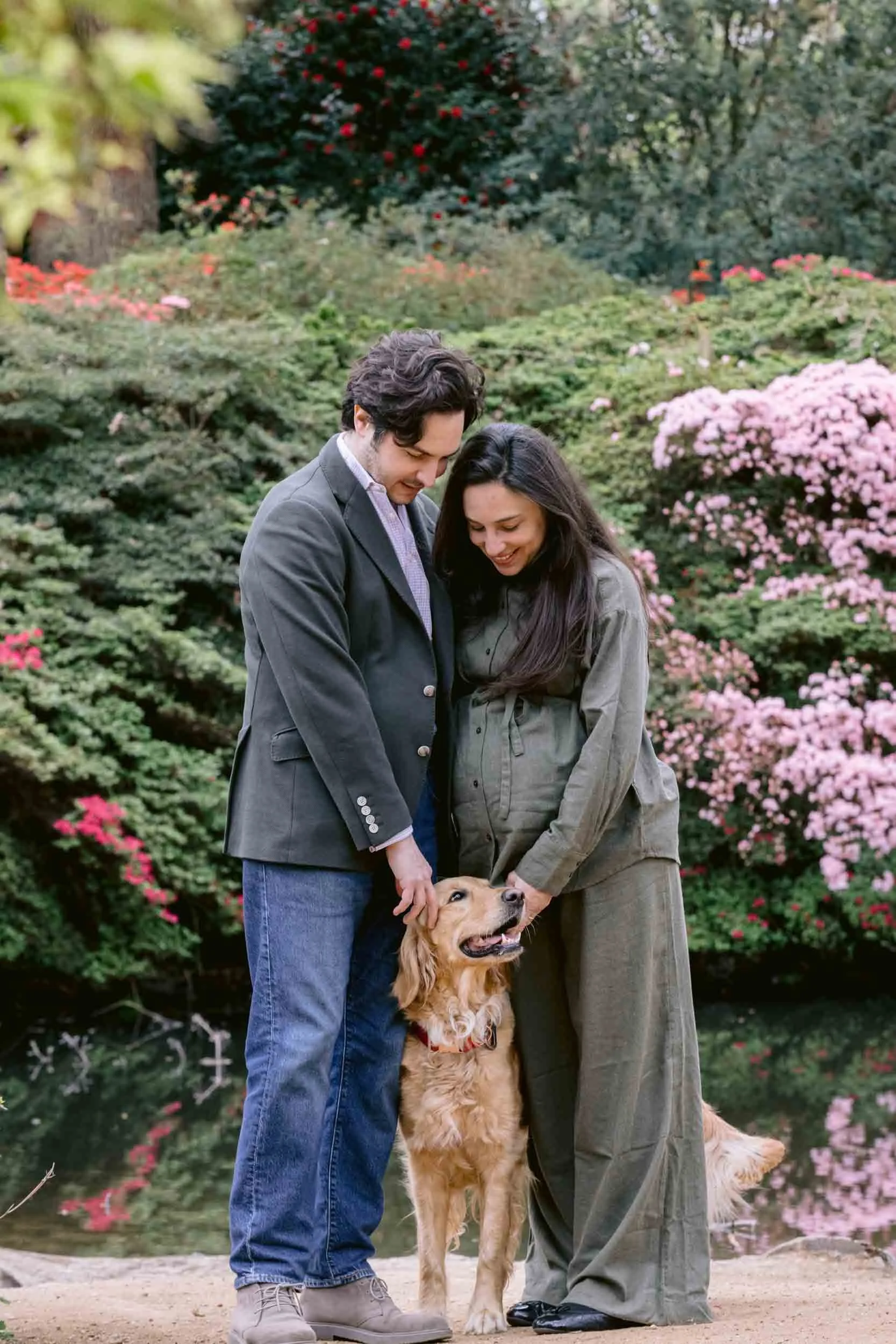 A couple expecting a baby stand with their dog in front of Still Pond in Isabella Plantation, London