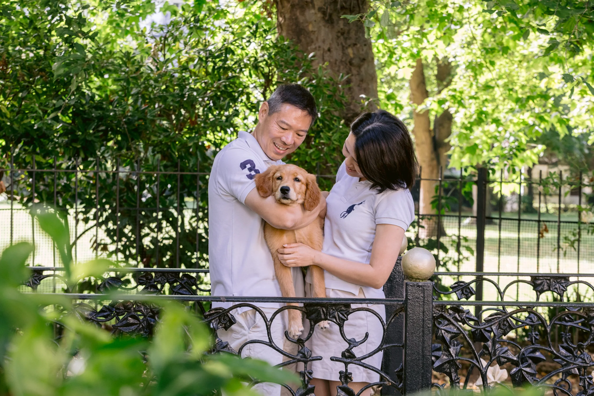 Couple standing on a bridge in a private garden in London holding a puppy during a photo session