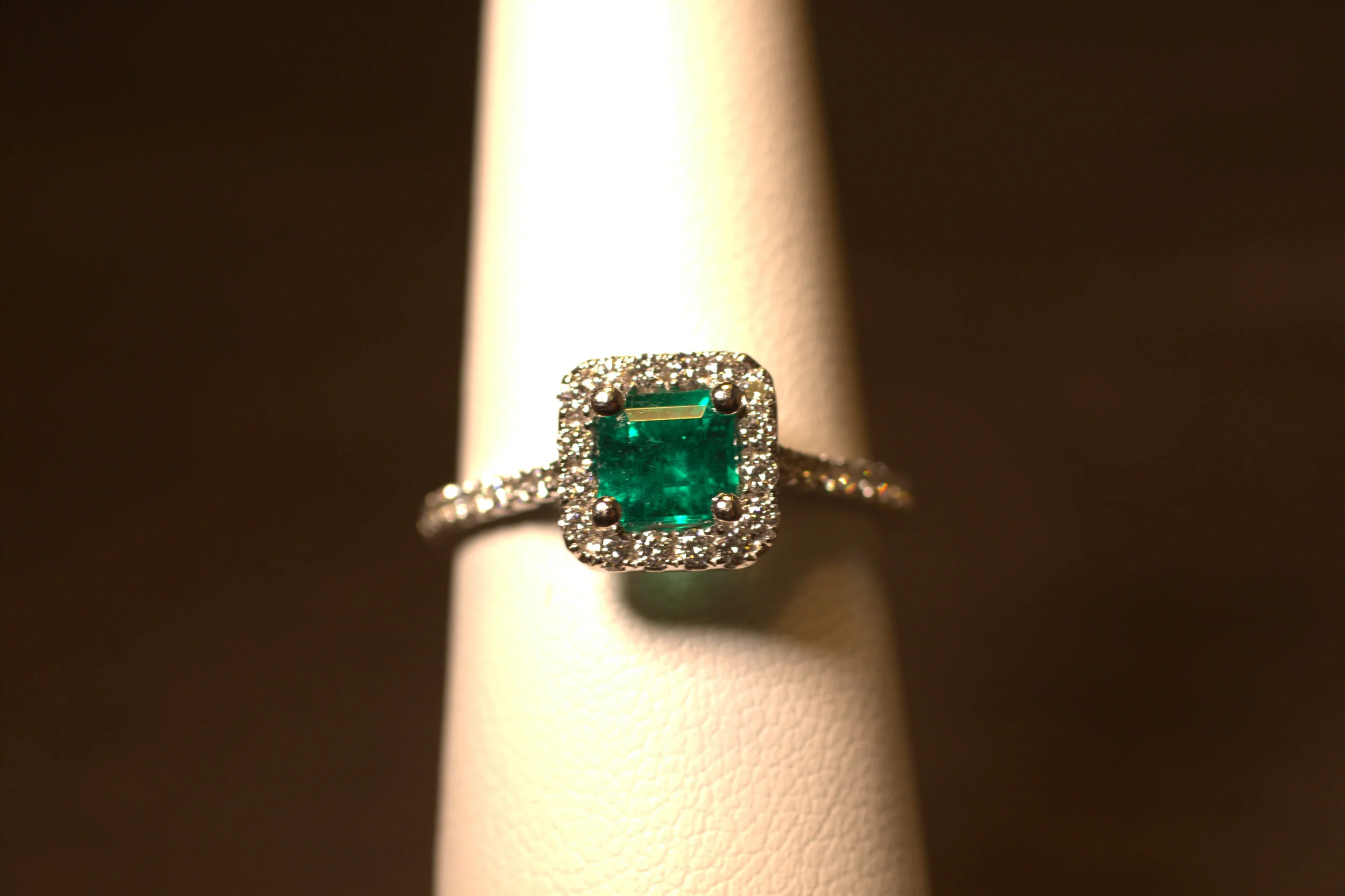 Platinum and diamond emerald ring. Square emerald cut emerald in a diamond halo with diamonds down the shank. Beautiful Columbian emerald displays rich green hues even throughout the stone. The emerald is set low into the halo to protect the gemstone. Great green color, the color of the year. $6000