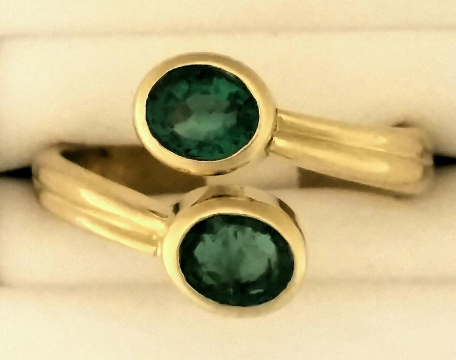Bezel set, oval emeralds adorn this 18K gold ring