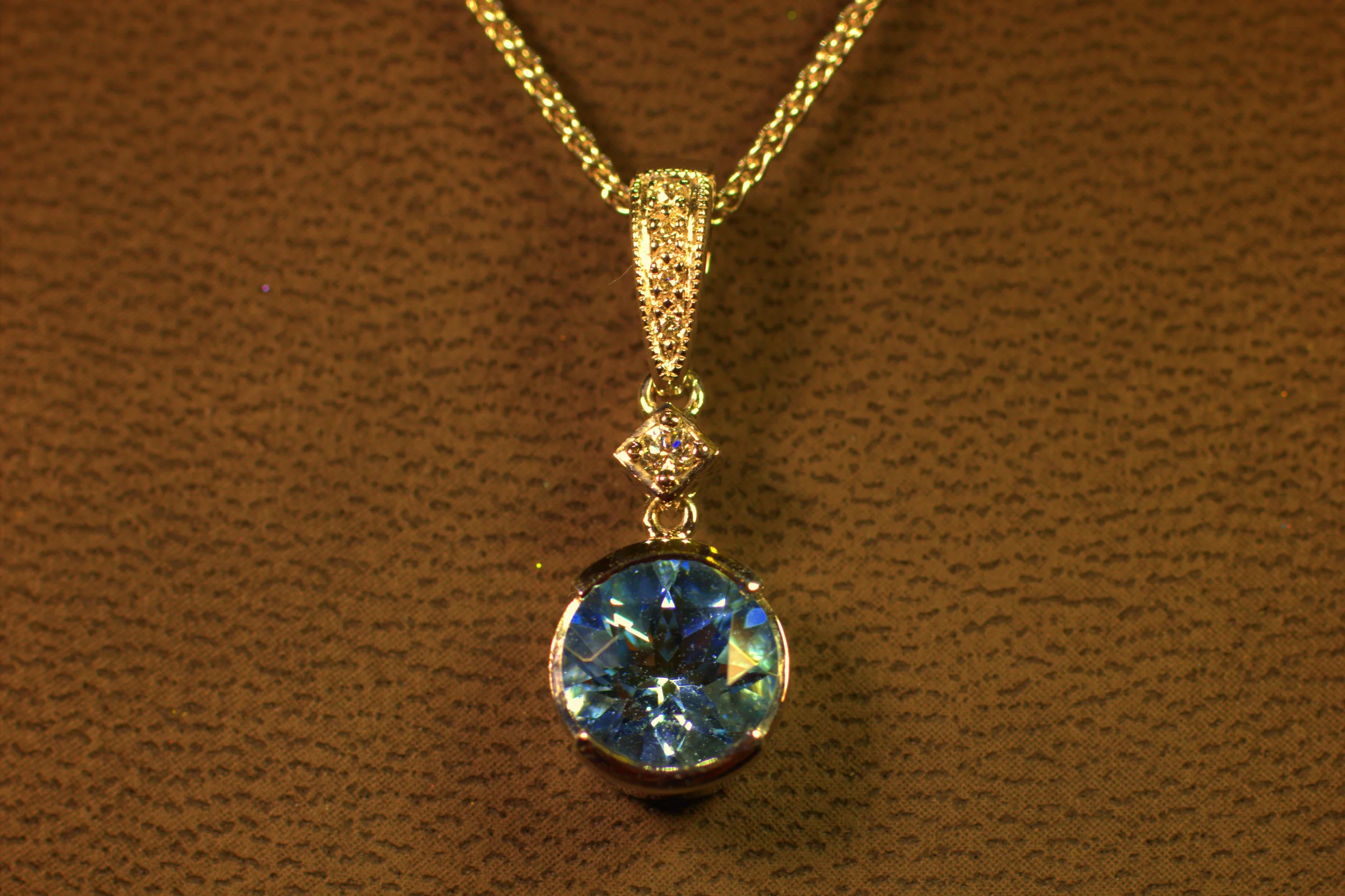 Half bezel pendant darker aquamarine with great fire diamond bail and a single diamond; lots of movement increases sparkle on the white gold pendant and chain. 