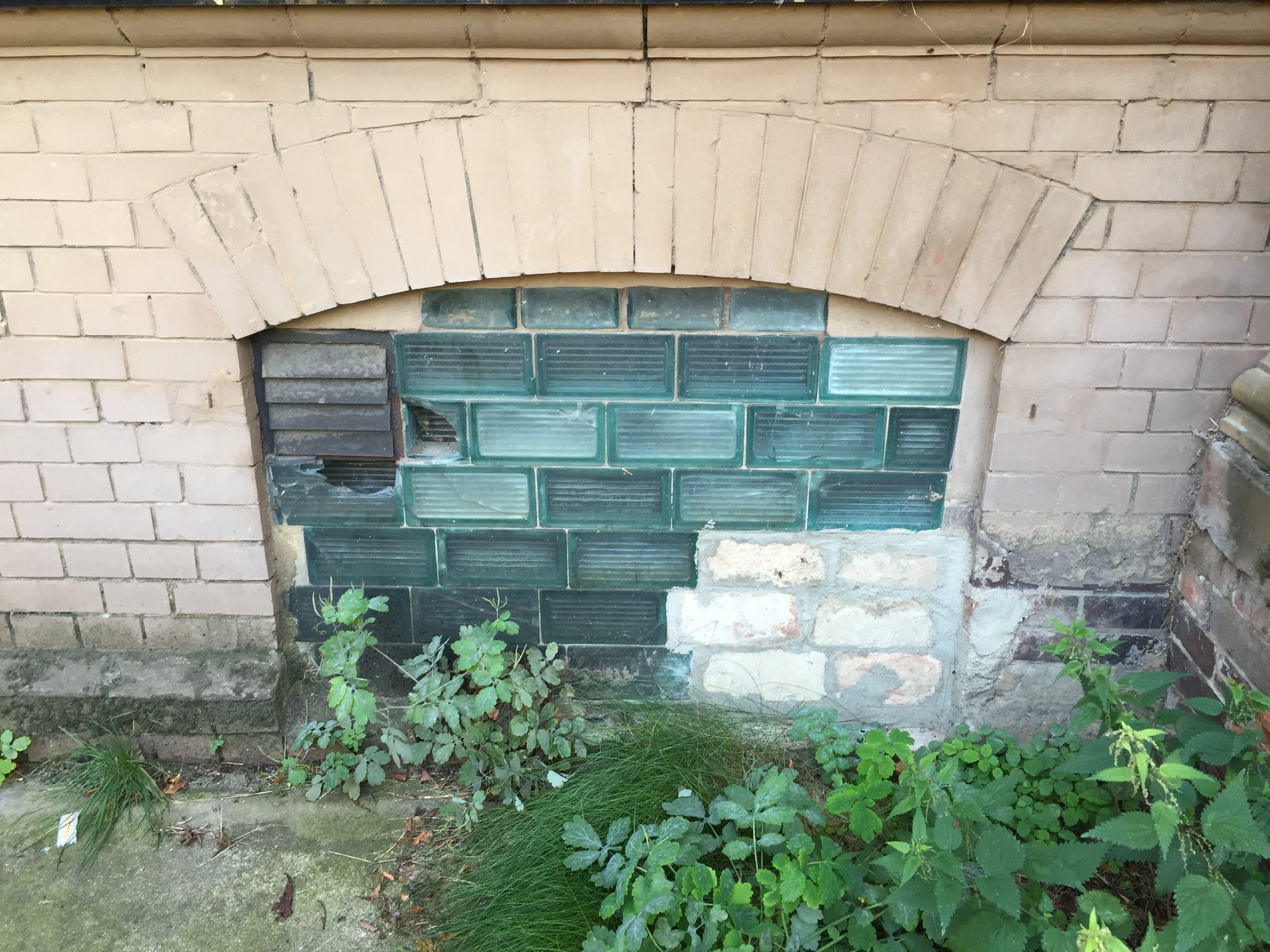 A basement window of House 3, sealed with multi-plated glass and bricks. The former detention cells are now used as administrative offices.