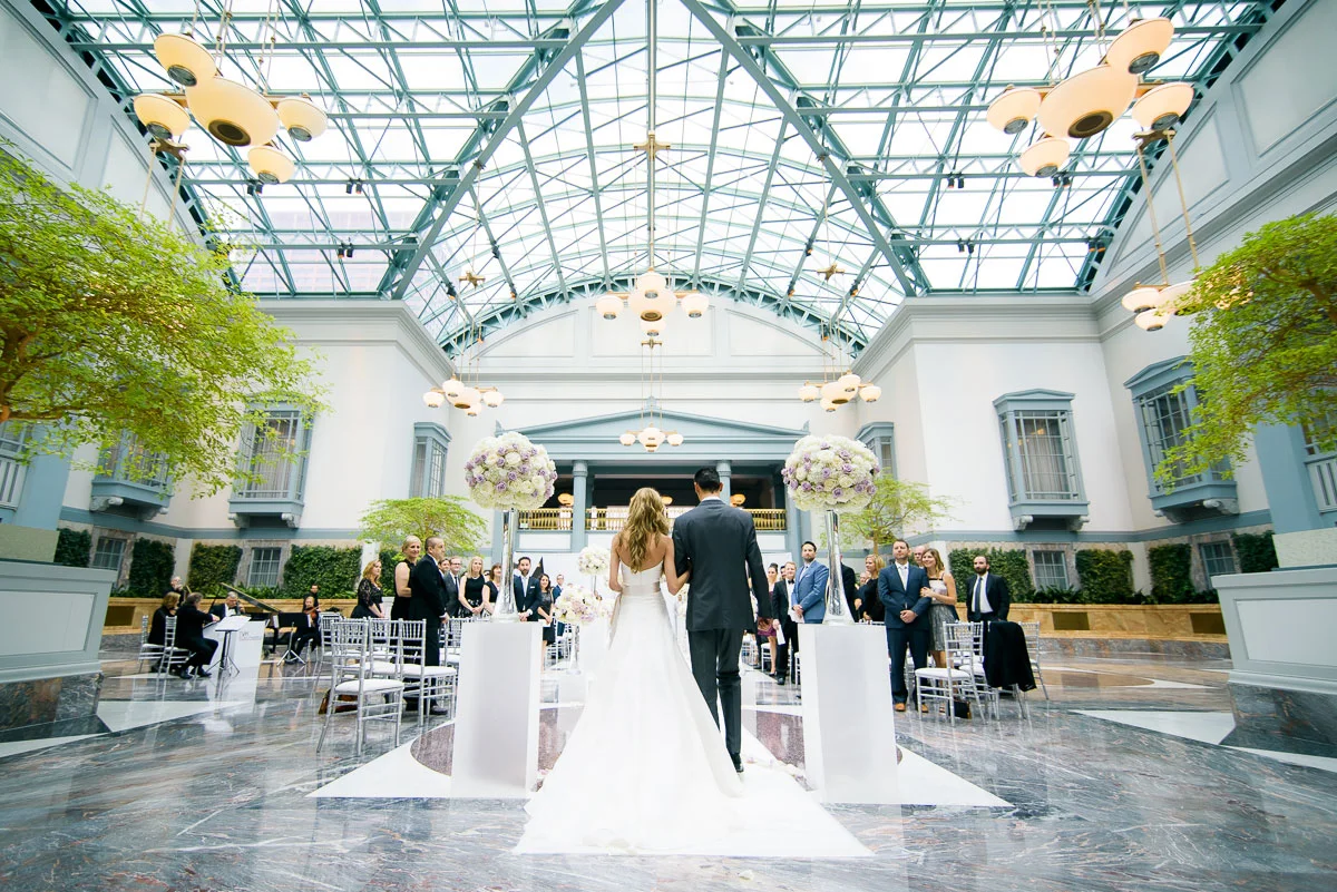 Bride walks down the aisle during a wedding at the Winter Garden in the Harold Washington Library Chicago.