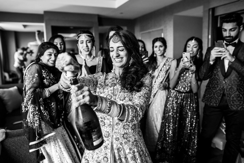 Brides pops the champagne during her Renaissance Schaumburg Convention Center Indian wedding.