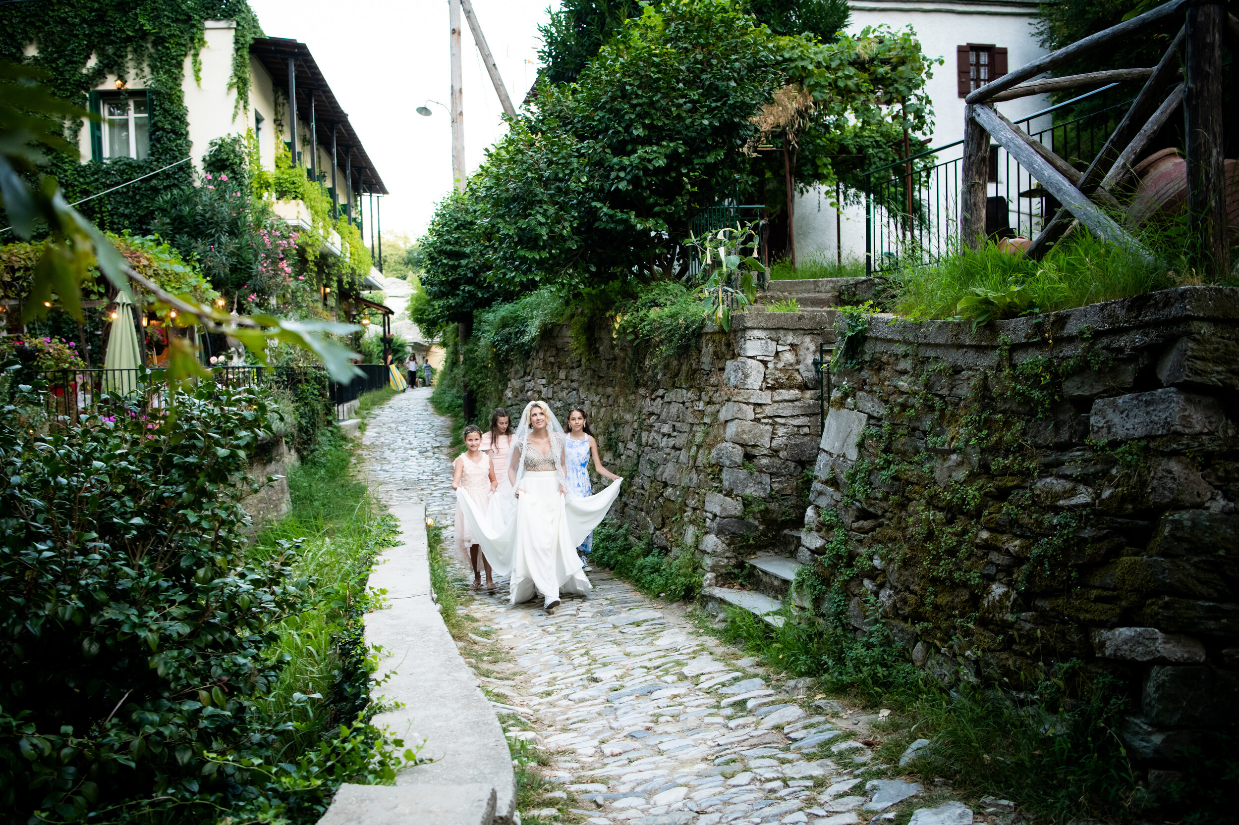 Bride and flower girls process down a cobblestone path to the ceremony:  destination wedding photo at the Lost Unicorn Hotel, Tsagarada, Greece by J. Brown Photography.