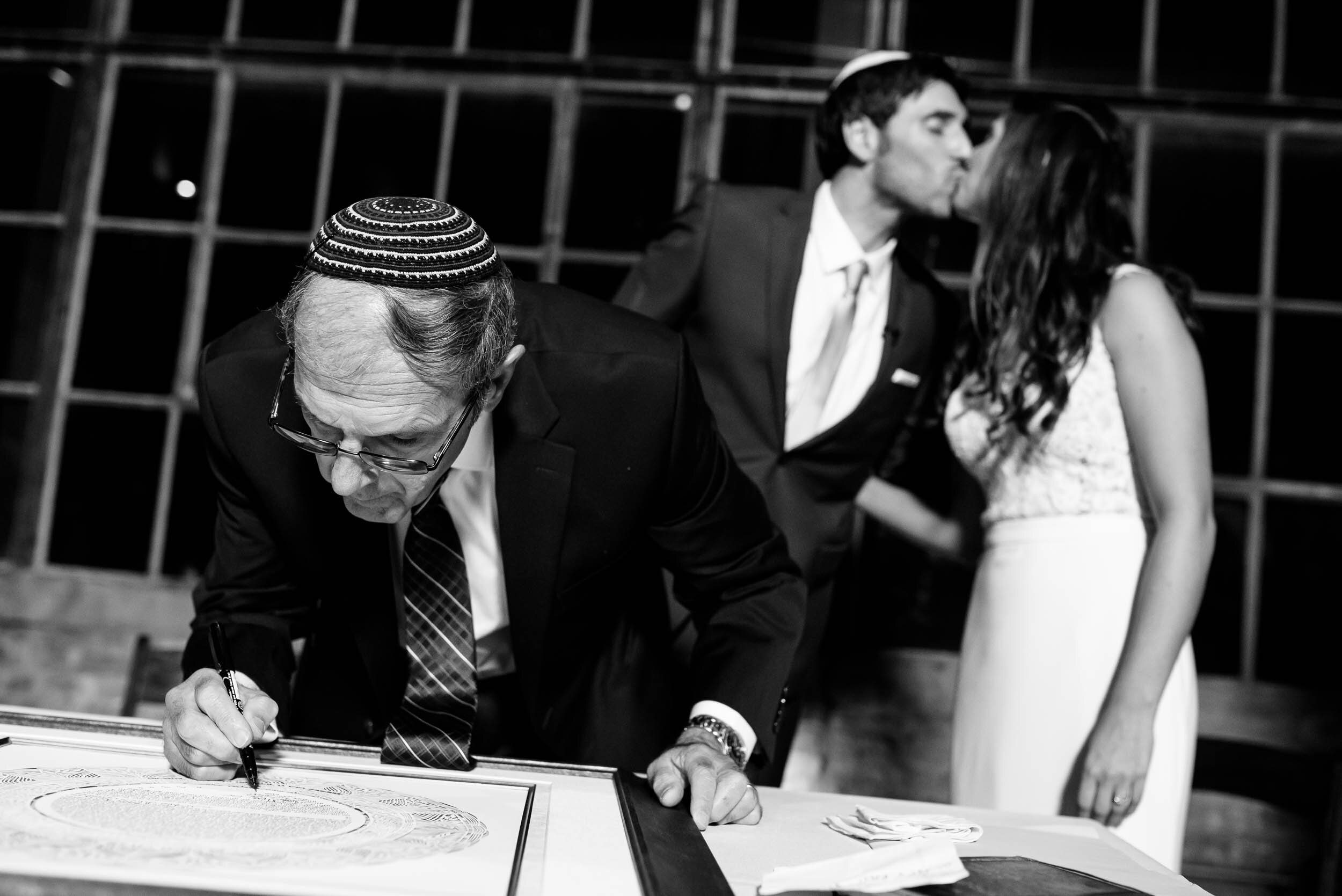 Couple kisses during their ketubah signing: Ravenswood Event Center Chicago wedding captured by J. Brown Photography.  