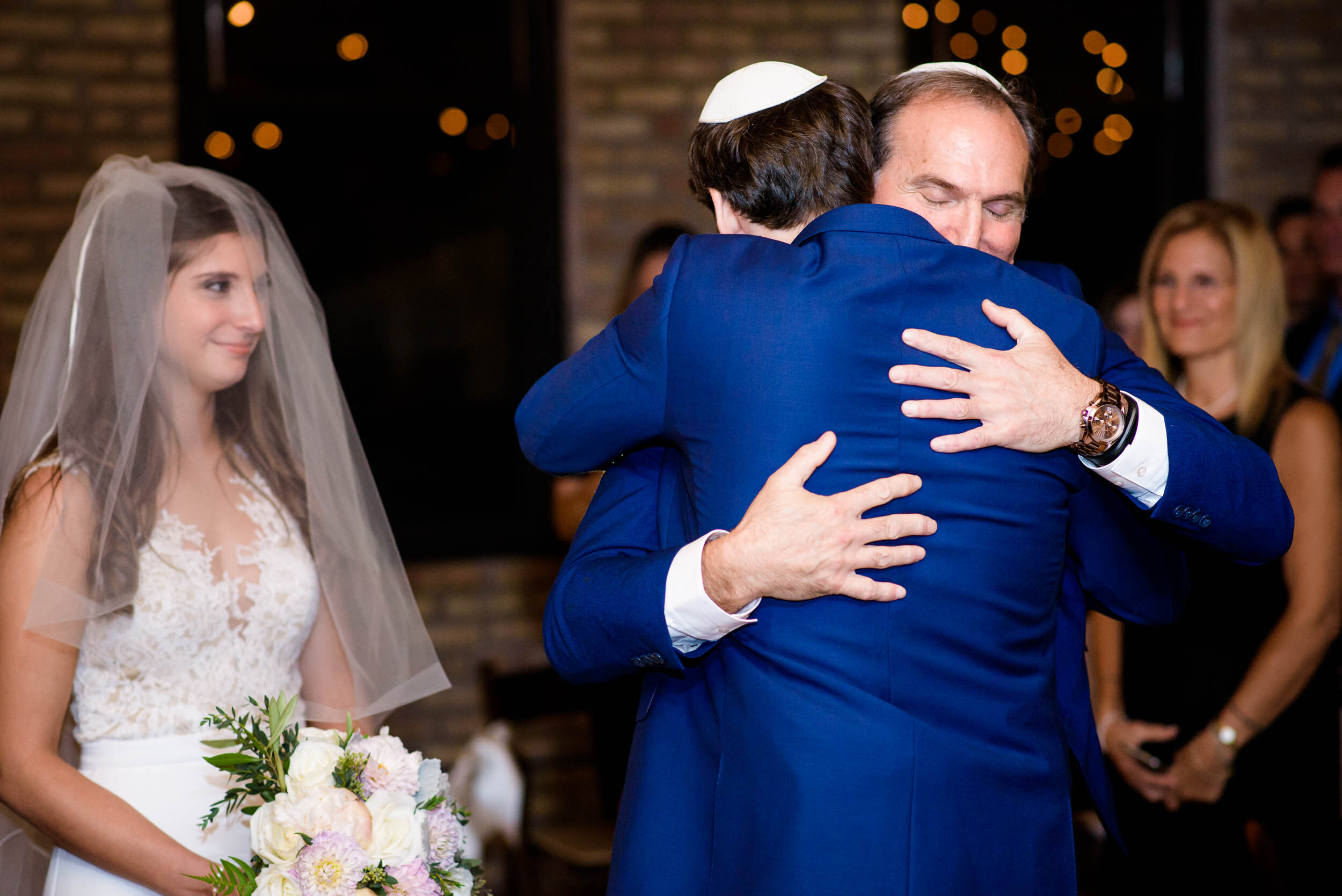 Father of the bride and groom hug during the ceremony: Ravenswood Event Center Chicago wedding captured by J. Brown Photography.  