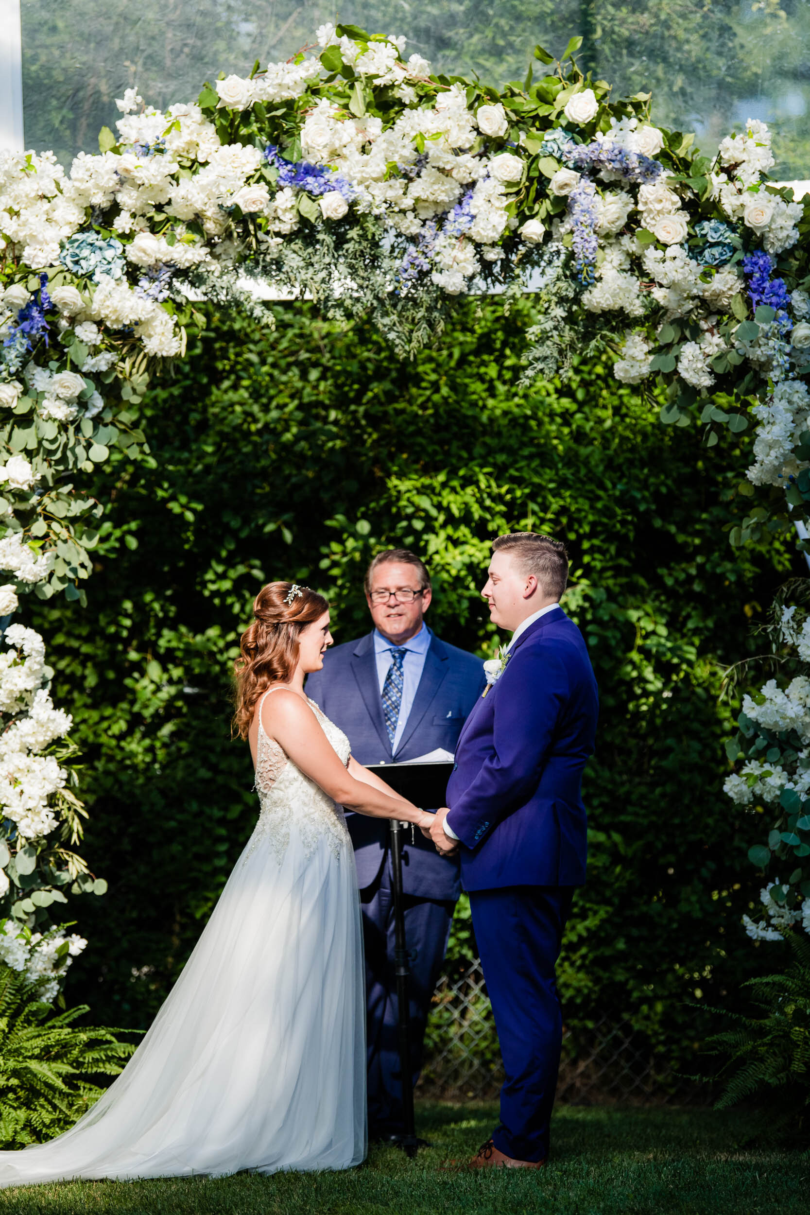 Bride and groom under the floral arch during their ceremony:  Chicago backyard wedding photographed by J. Brown Photography.