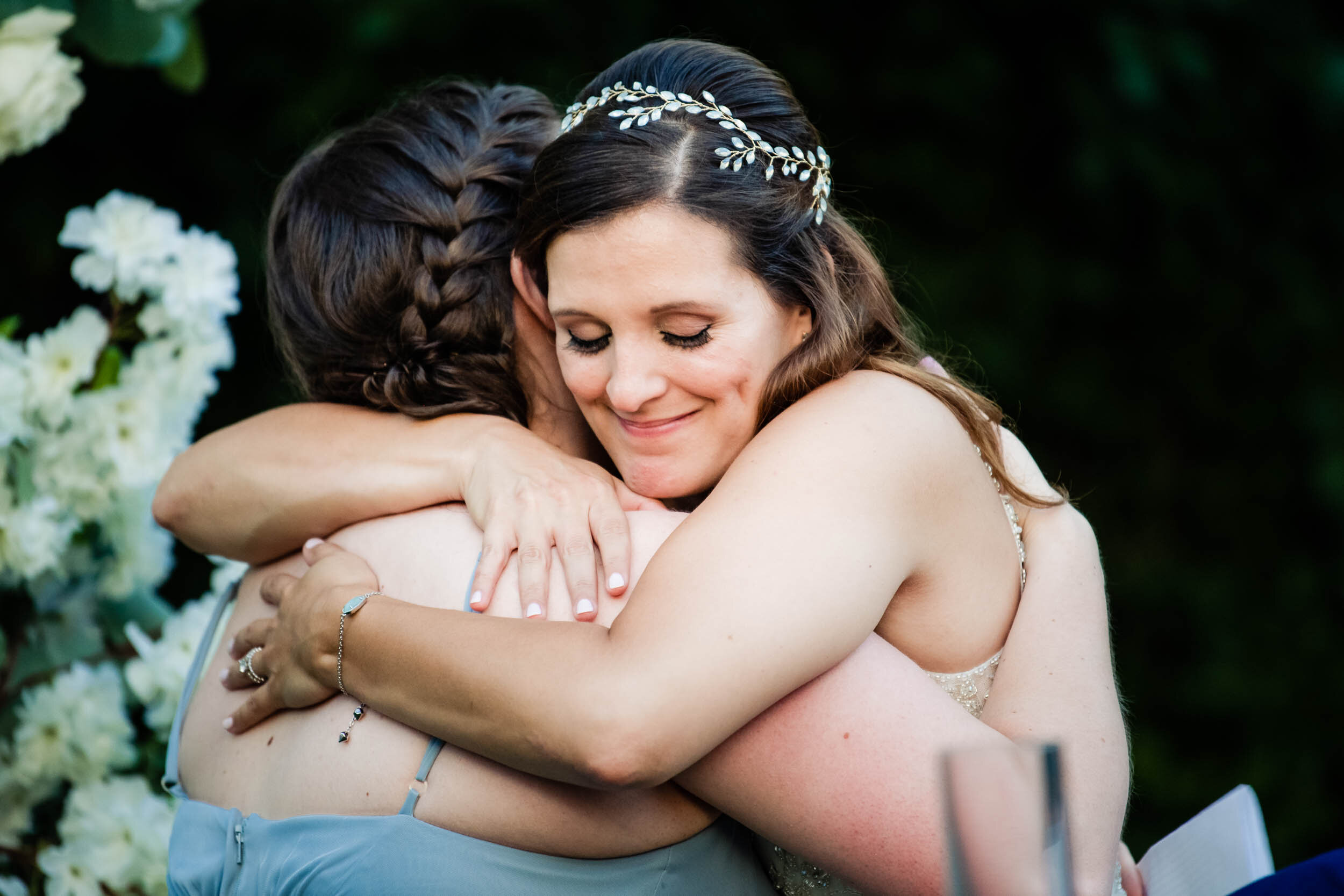 Bride and maid of honor hug during the reception:  Chicago backyard wedding photographed by J. Brown Photography.