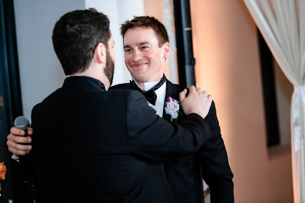 Groom and best man embrace during a reception at the Stockhouse:  Chicago wedding photographs by J. Brown Photography.