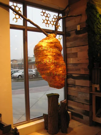The hive from inside the store. I created the shape of the hive with chickenwire. I then covered the entire structure with strips of shellacked tissue paper (shellacking the paper gave it an amber color and a pretty semi-translucence). For some cheeky fun, I also incorporated wrappers from Bit O’ Honey candy into the hive! Click on for a detail shot… 