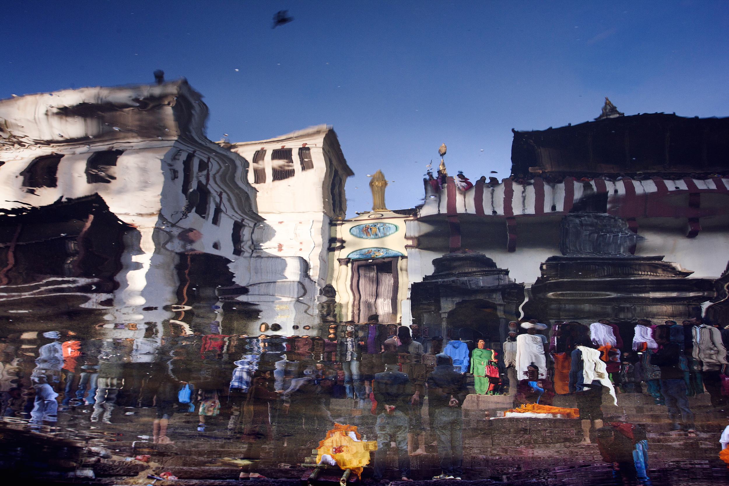 Two bodies (in orange) are laid out on the eastern ghats for purification in the Bagmati River. Friends and family of the deceased pray, and say their final goodbyes. 