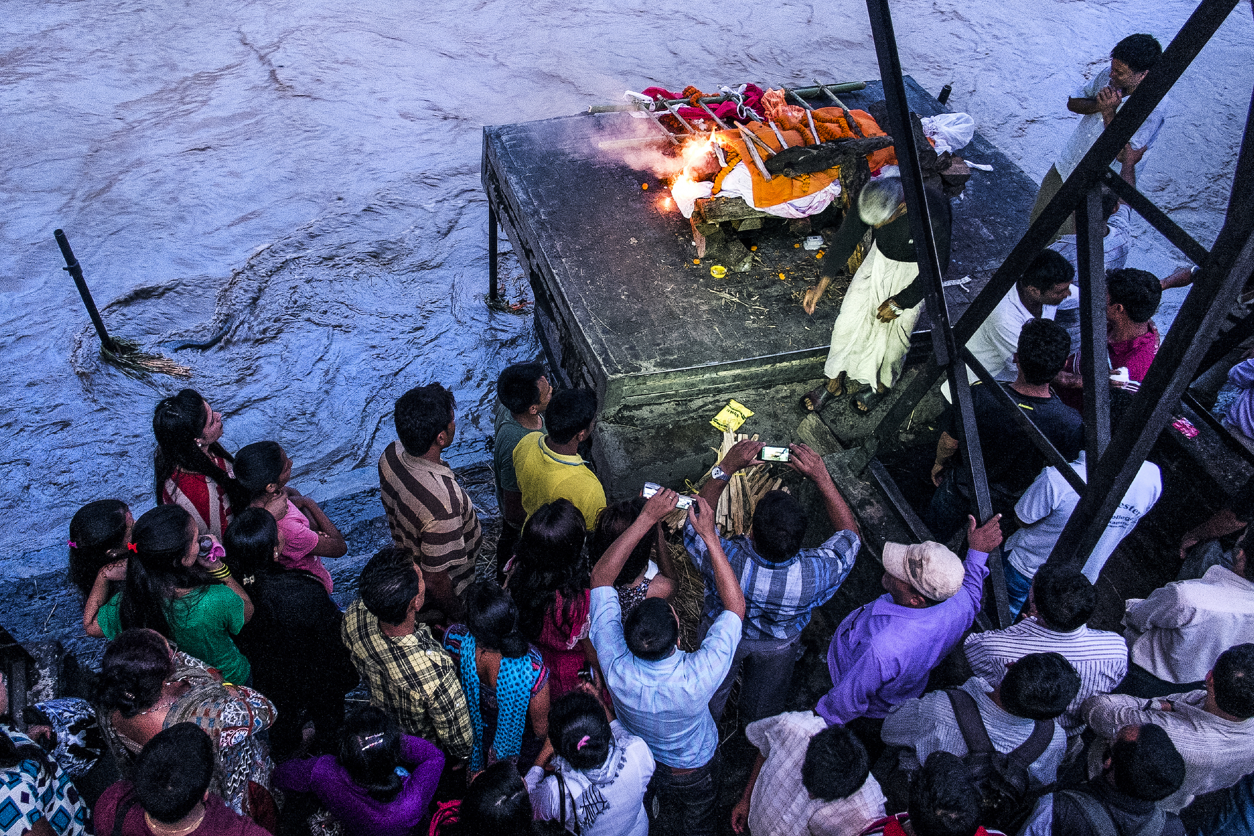 Relatives film the beginning of a cremation of an elderly man at Pashupatinath's northern ghats. 