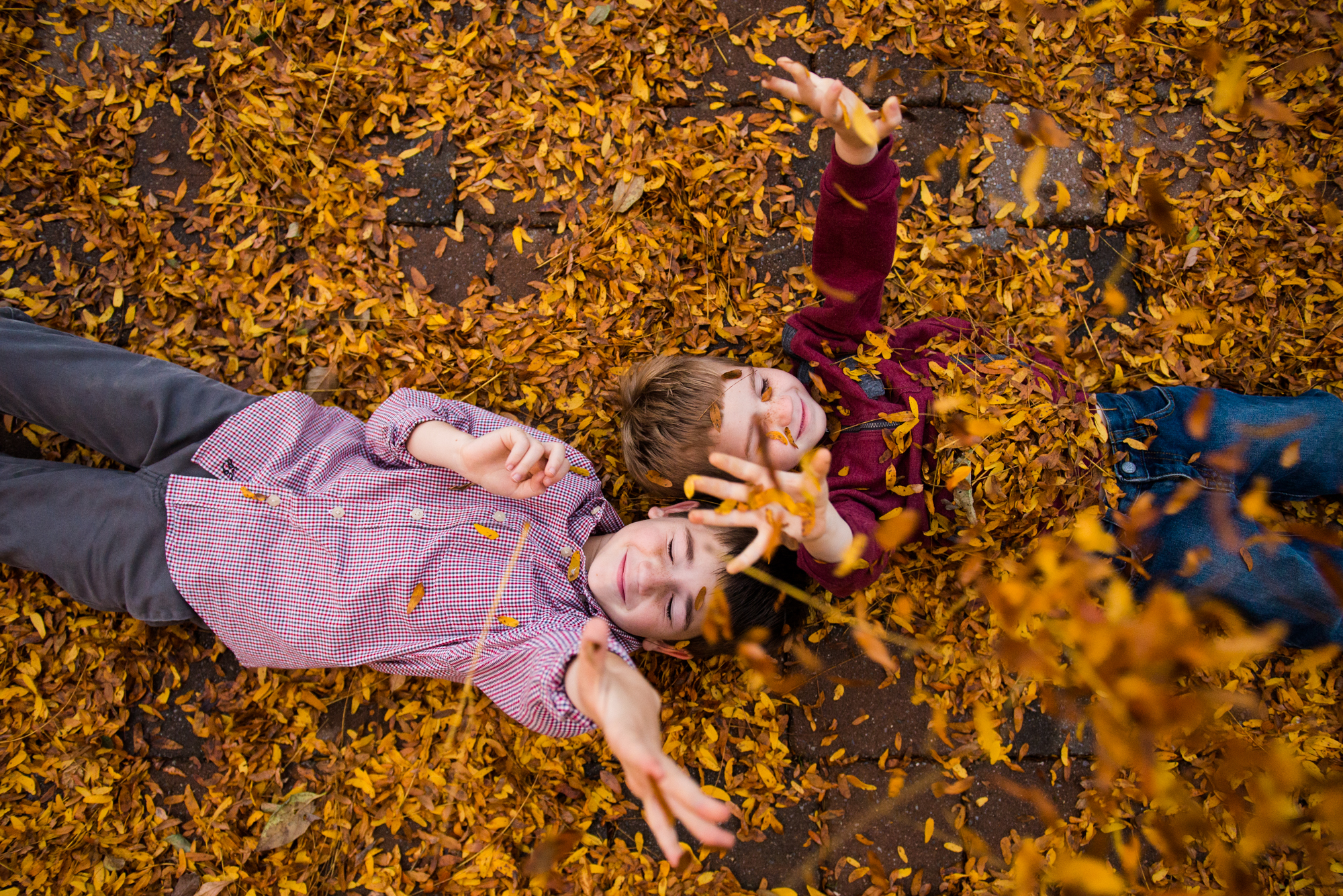 Two boy lay in fall leaves while tossing them into the air during a family photo session