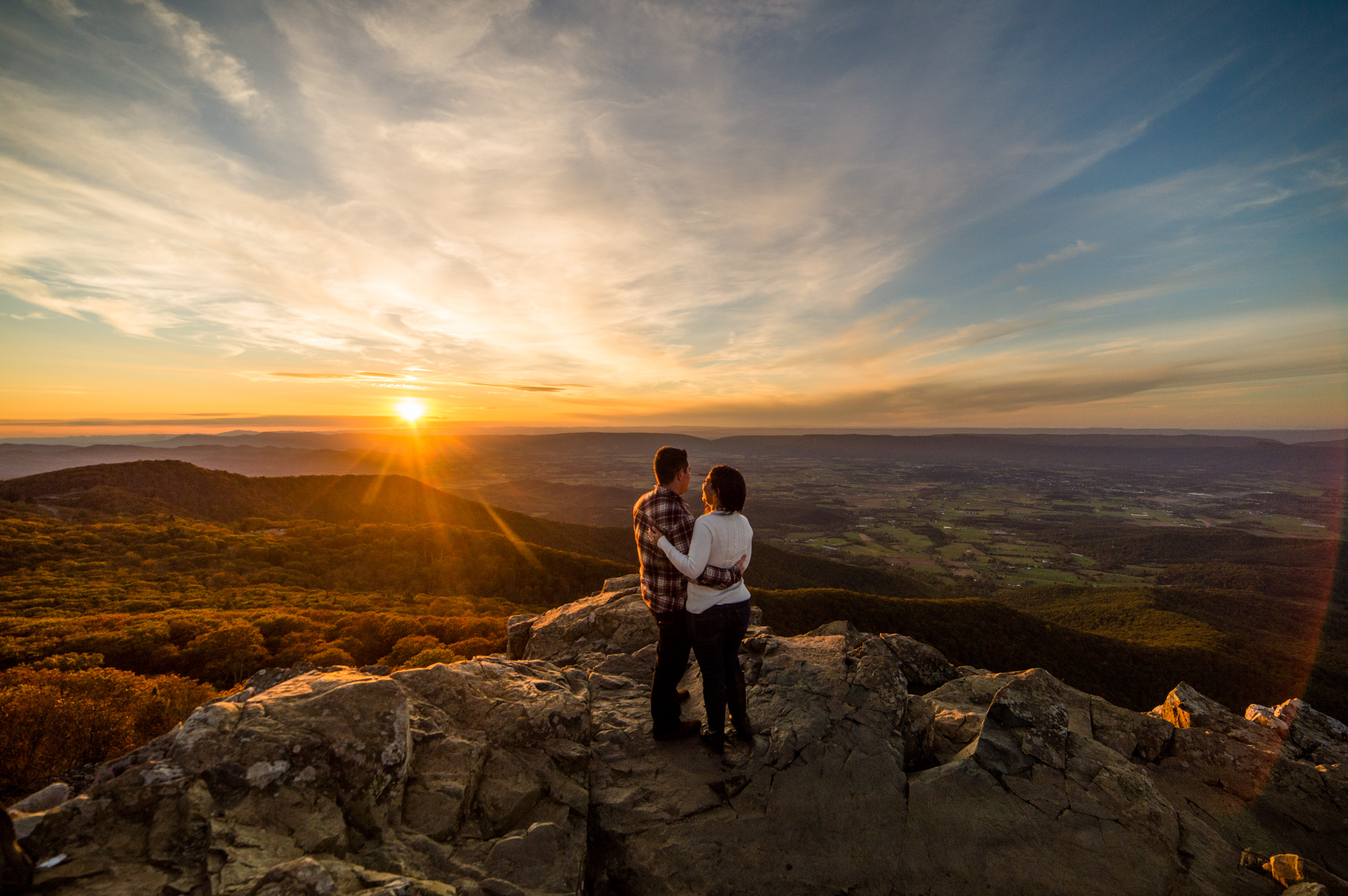 A couple stands on a mountain overlook at sunrise