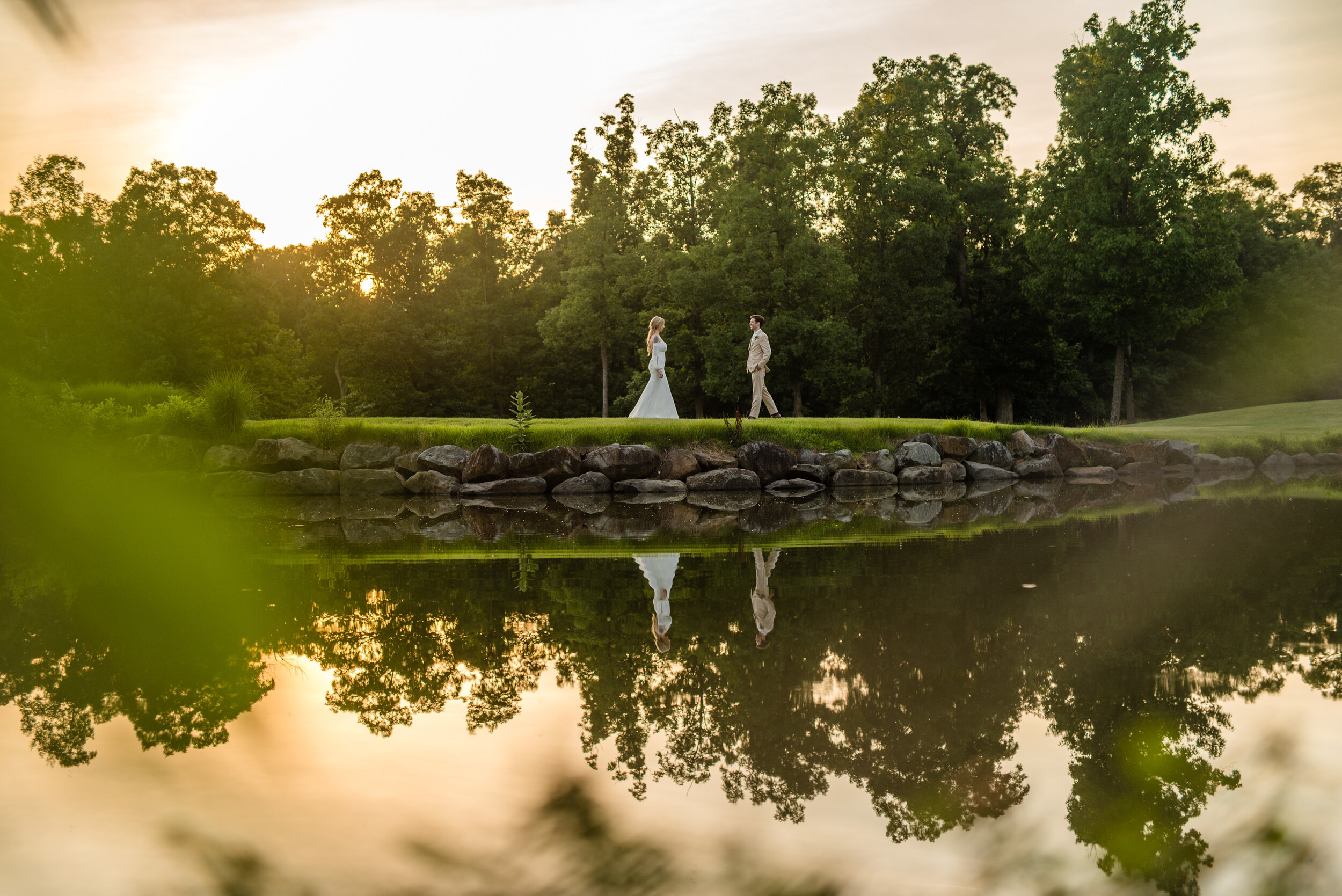 A bride and groom walking towards each other at golden hour  reflected in the pond