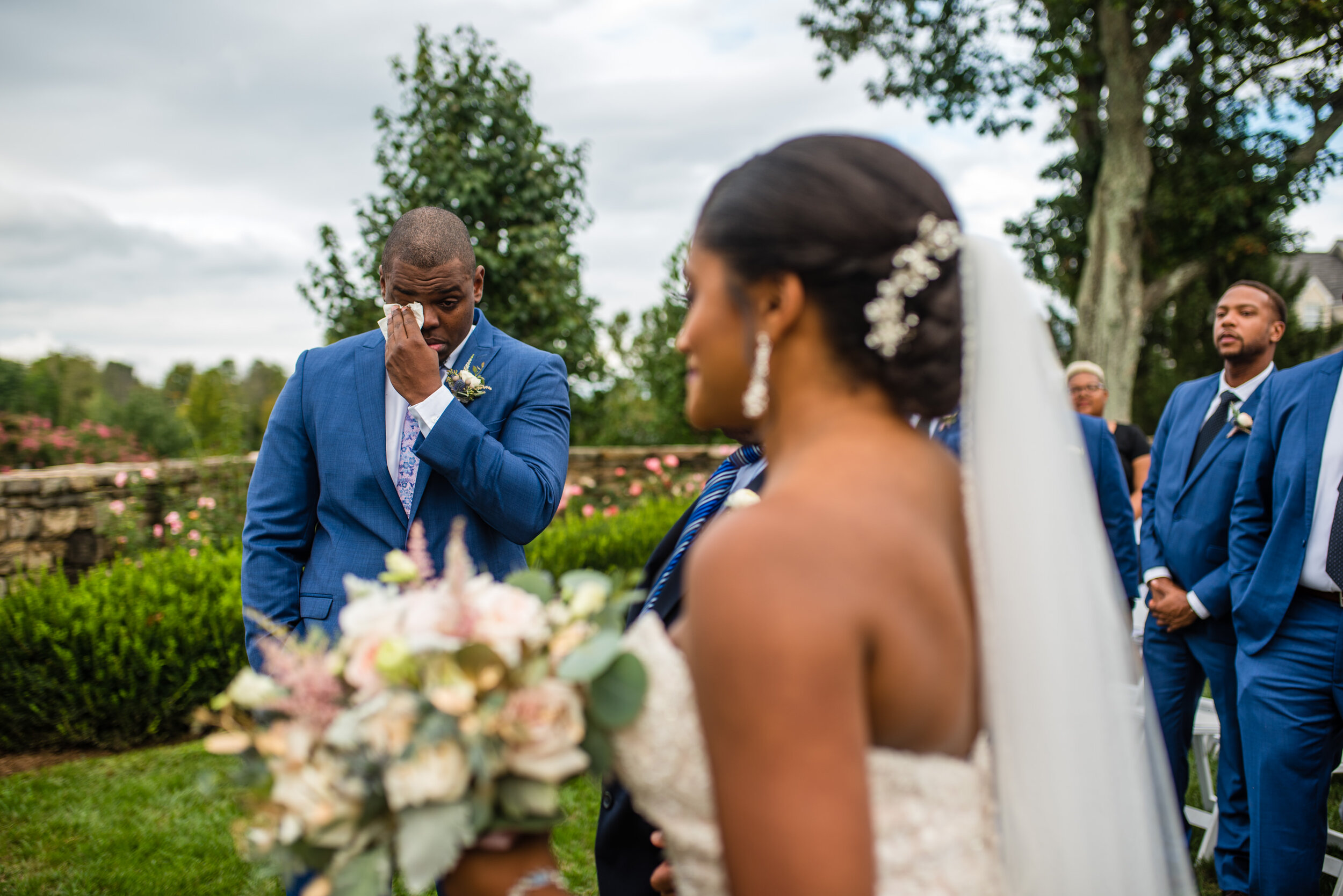 A groom wipes away tears as his bride approaches