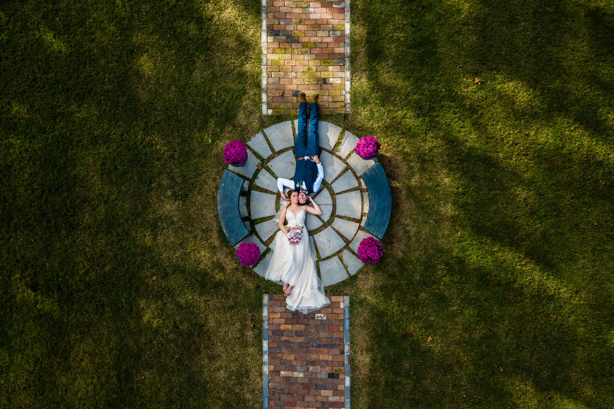 A couple laying head to head on a stone mosaic in their wedding clothes