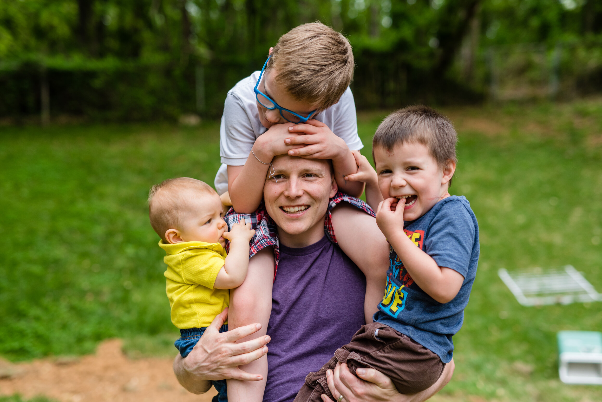 A father holding his three sons, one on his shoulders and one in each arm. 