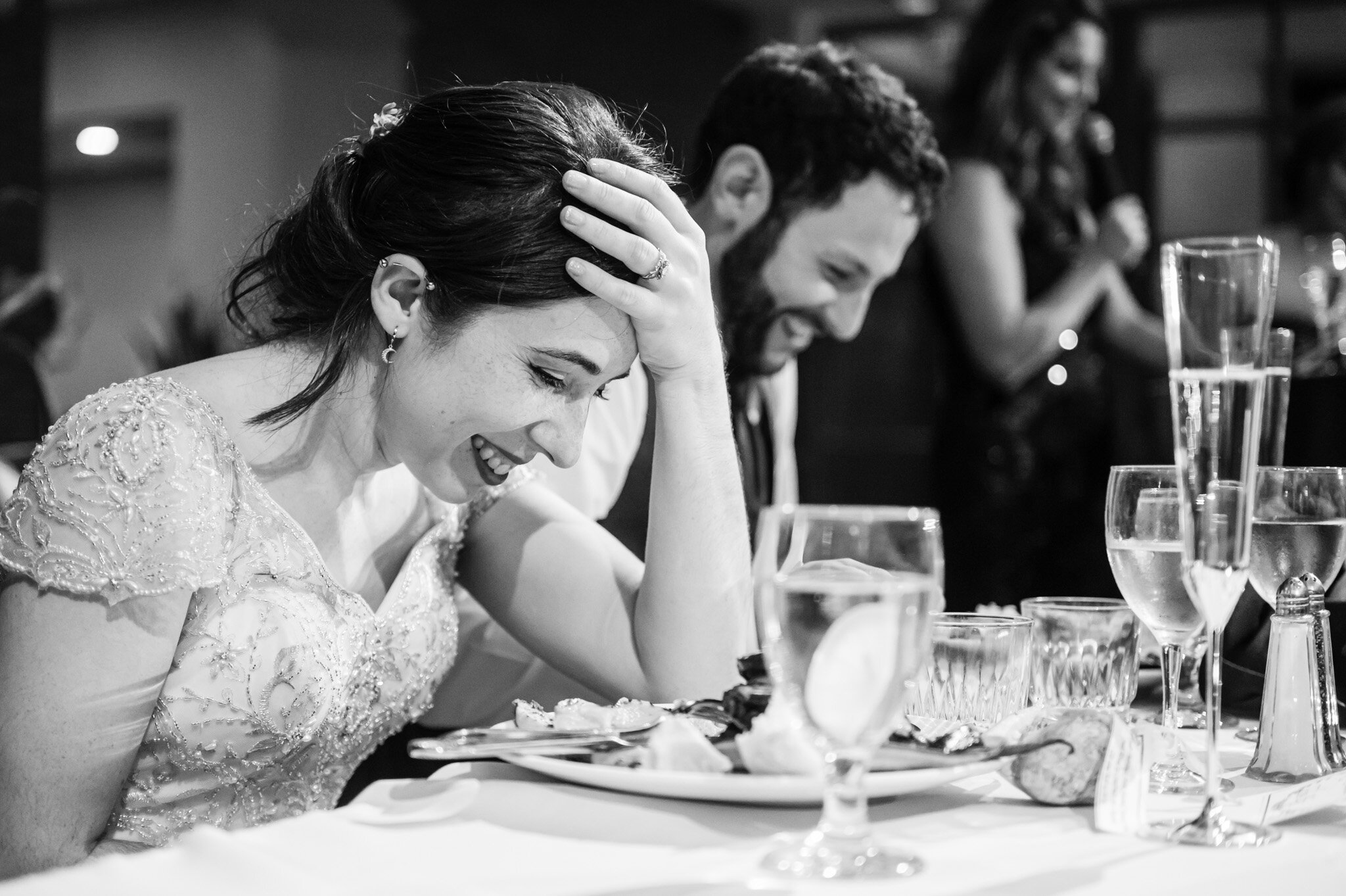 the bride and groom laughing at a speech at their wedding reception