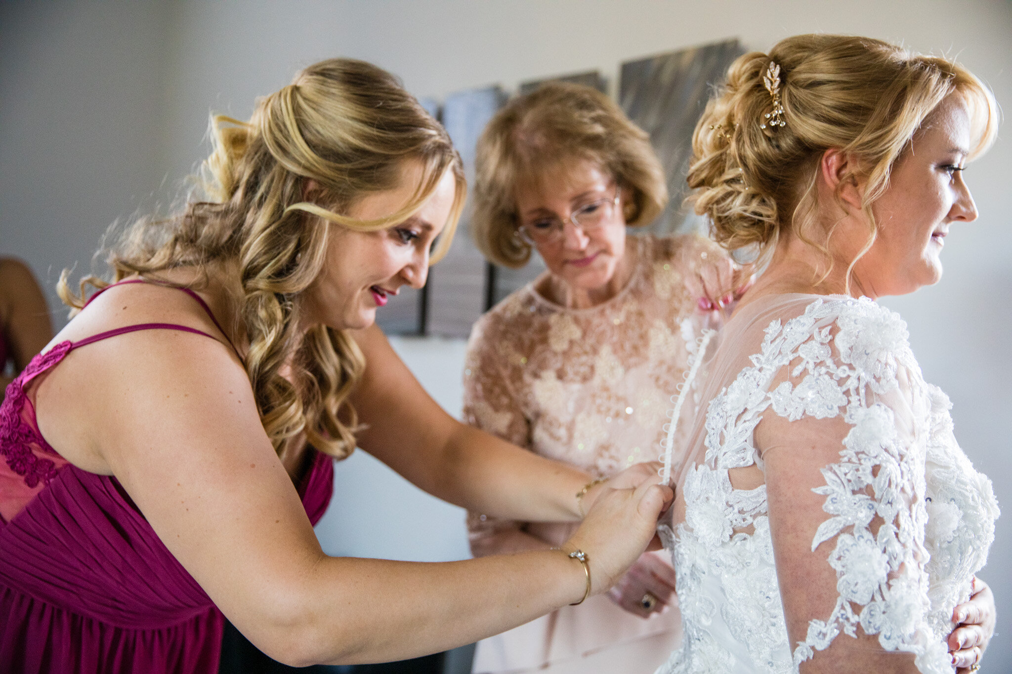Bridesmaid helping the bride to finish putting on her dress