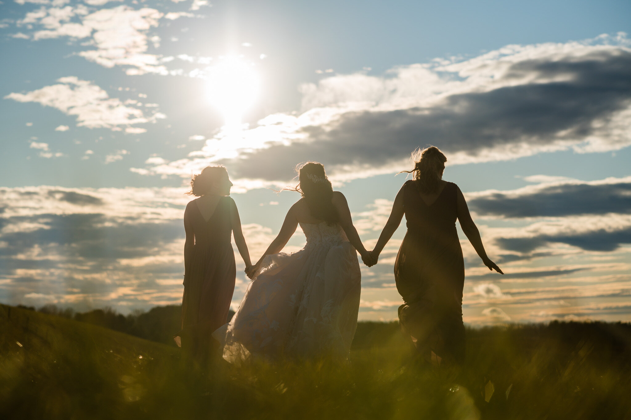 A bride and her two bridesmaids walking together in a field