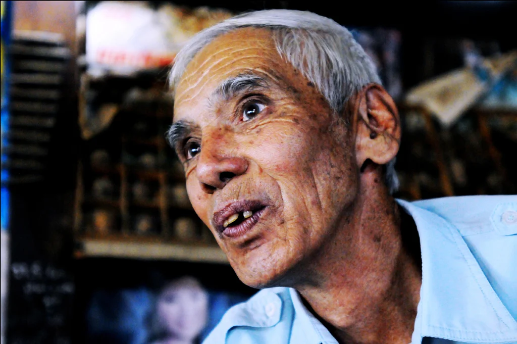 Grandfather Kampouvieng explains how for the first 3 years of the war he hid underground and
as his frustrations grew, he decided to fight. He was a French language teacher for many years
and he now owns a shop where he exhibits bombs to educate the youth of their dangers. Xieng
Khouang Province, Laos