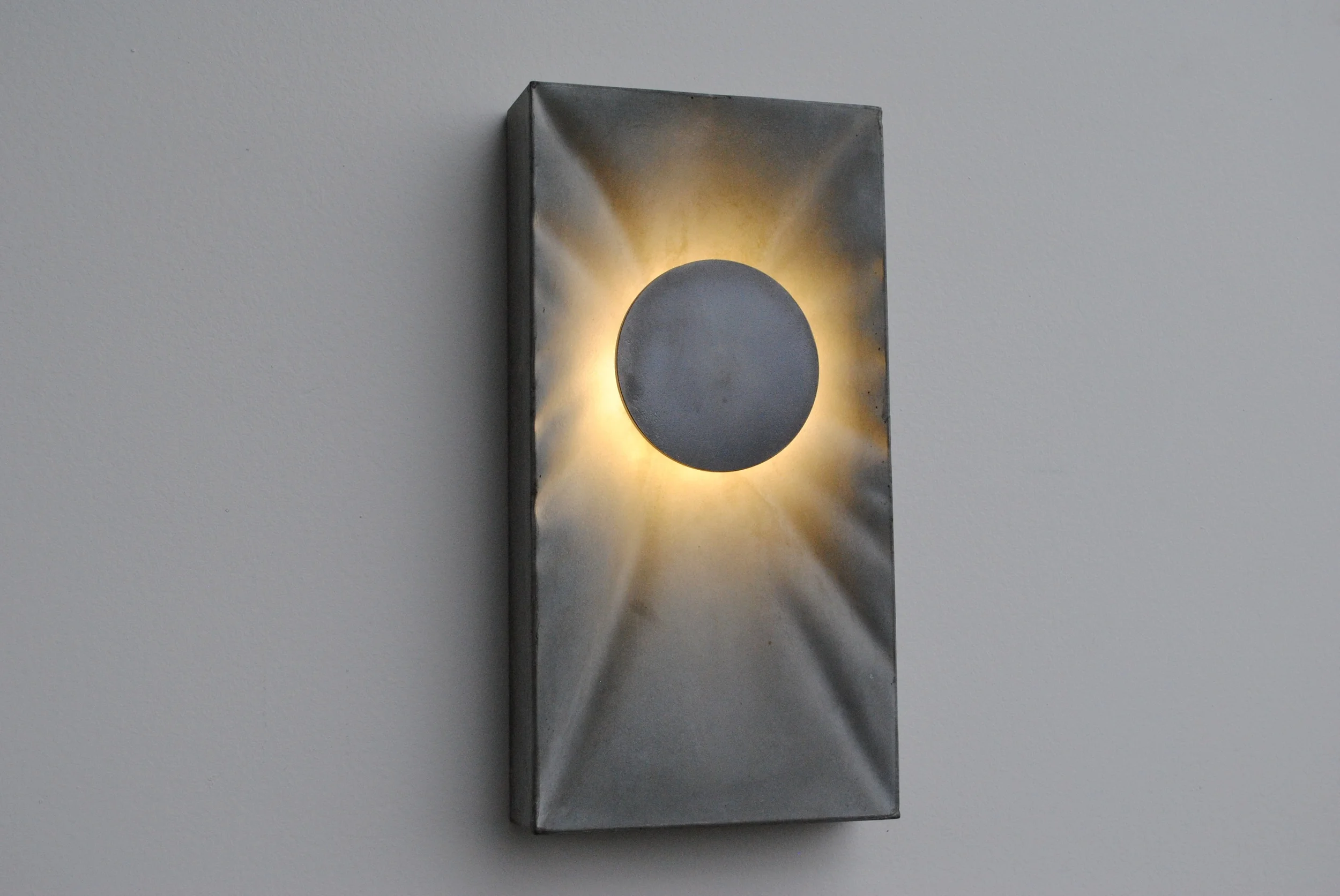  Eclipse Sconce in natural color; steel and concrete meet light.&nbsp;The steel disc acts as a diffuser for high efficiency LED light and spreads it out over the varied concrete backdrop. &nbsp;7"X13.75"X2" and less than 6 lbs. 