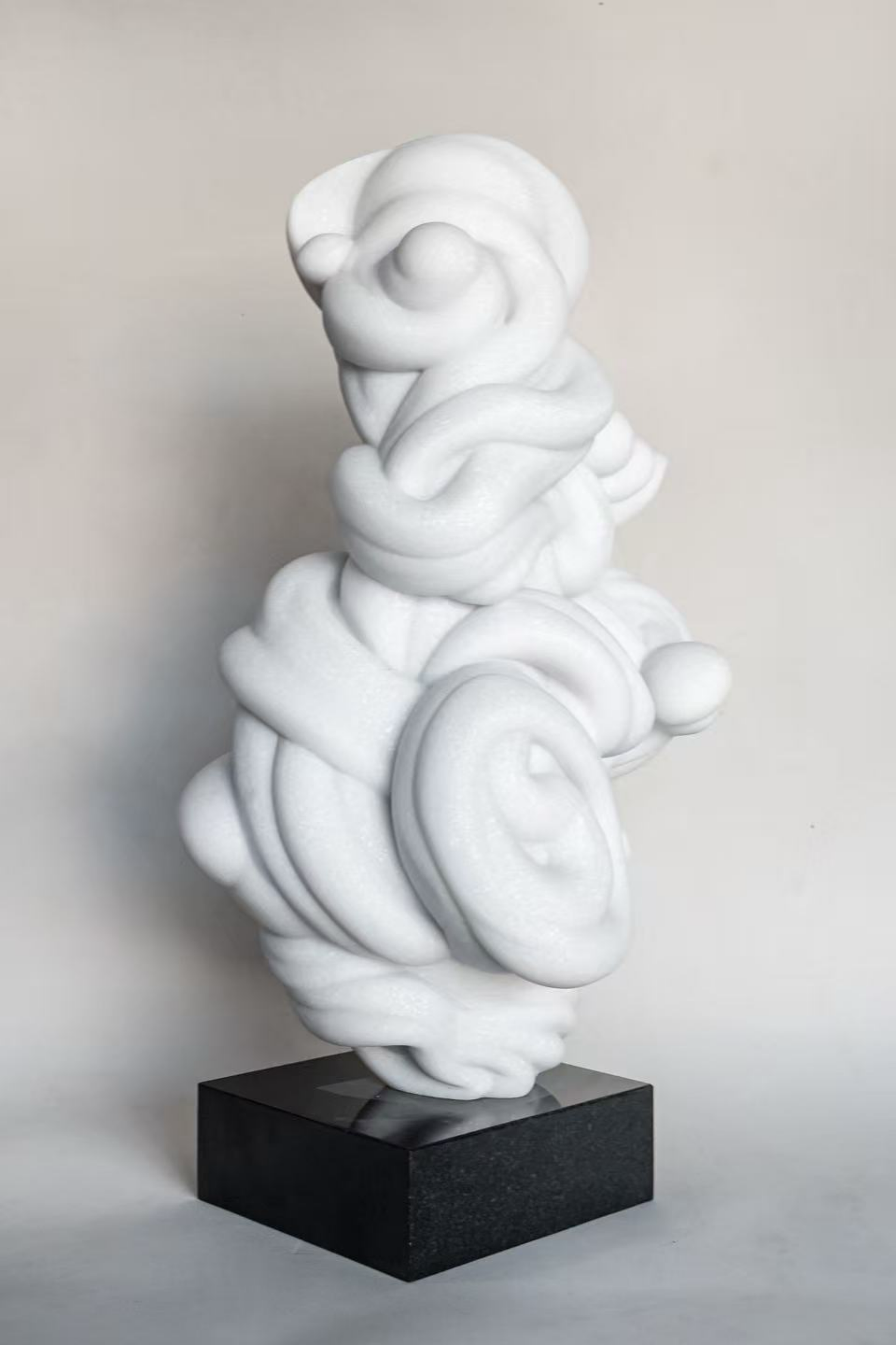 White abstract sculpture with swirling shapes on a black rectangular base.