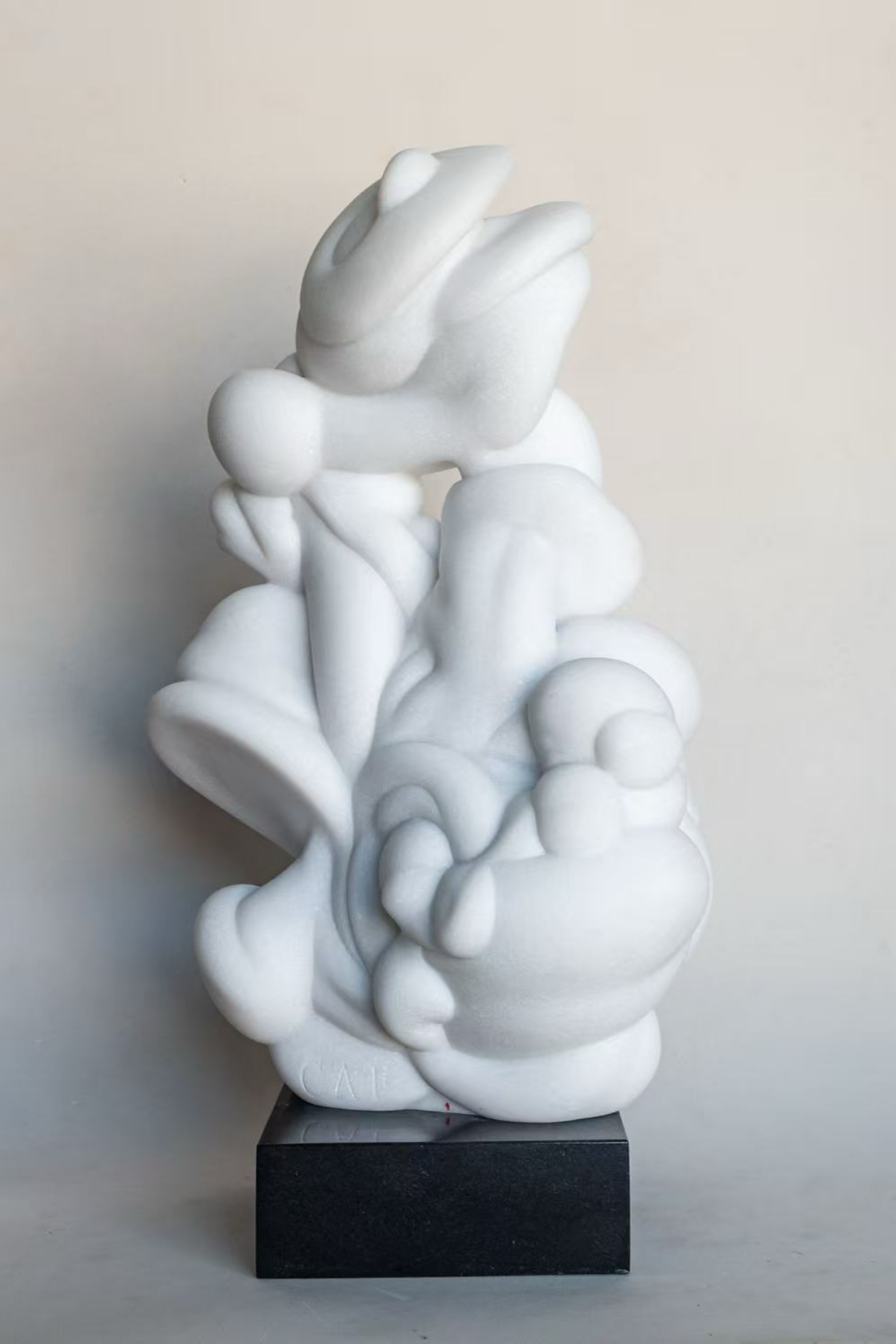 Abstract white sculpture of intertwined human figures on black base.