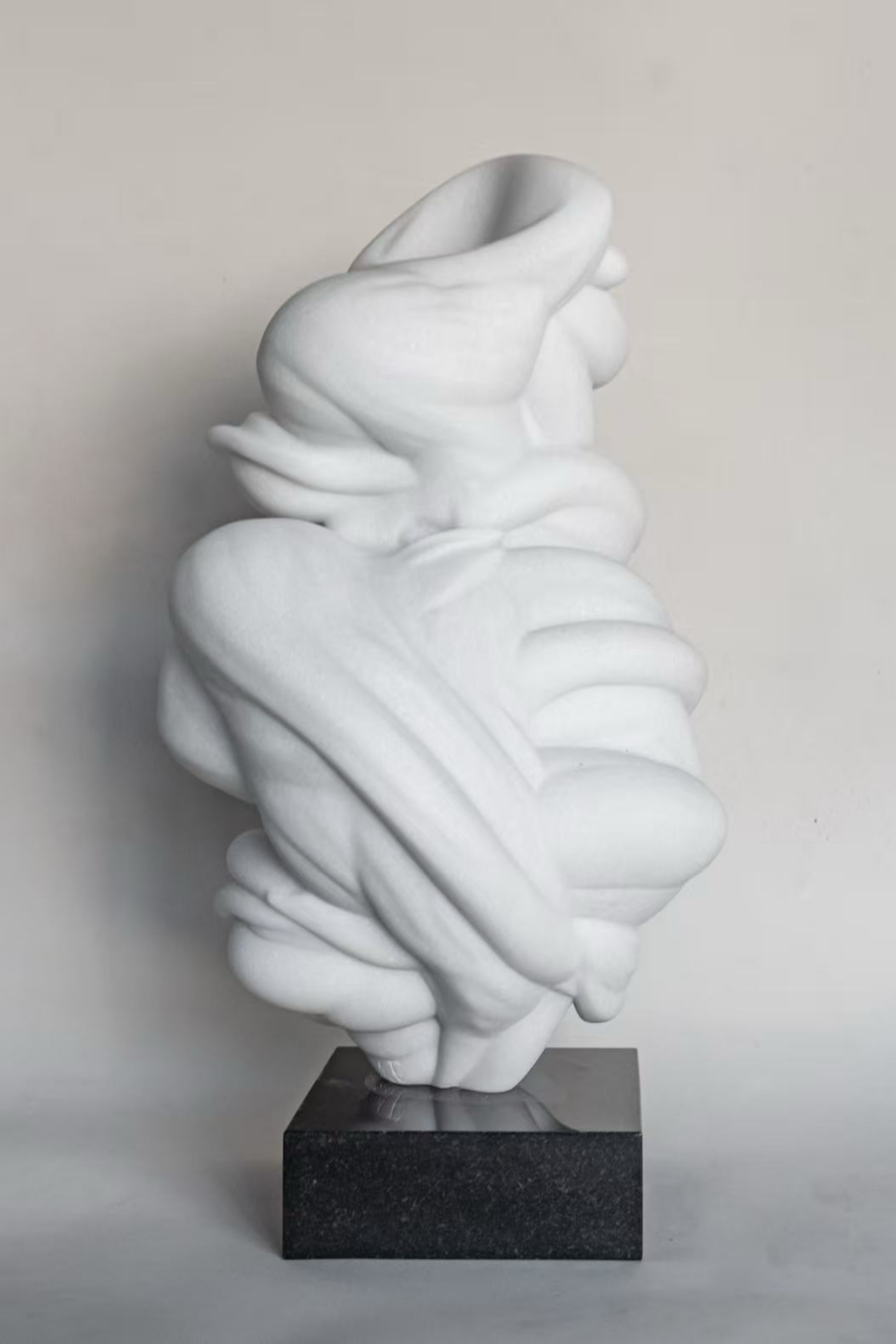 Abstract white sculpture with flowing, layered forms mounted on a black rectangular base.