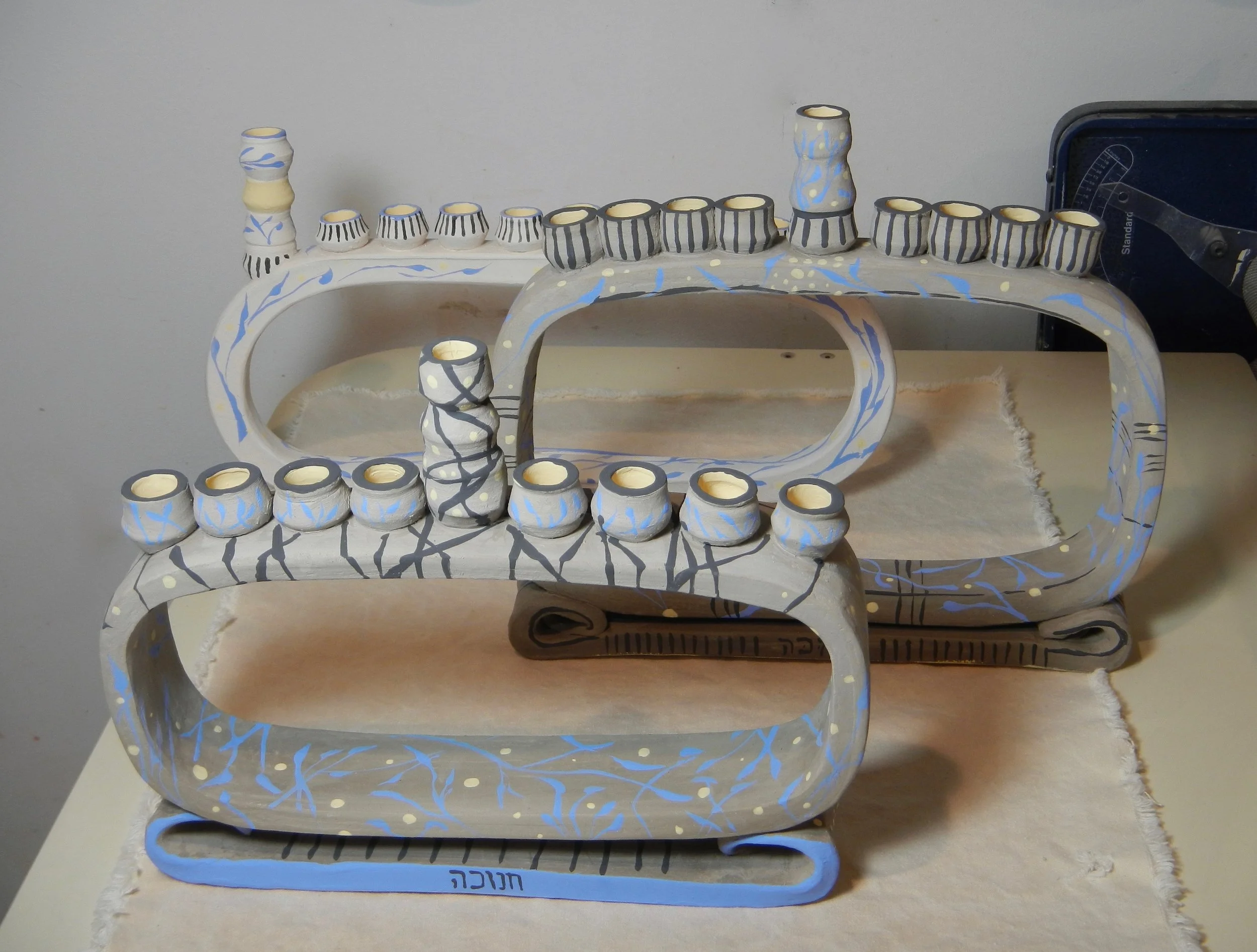 (The front one is the same as pictured in the previous photo, with some brushwork. (photo Mimi Stadler 2016) Due to my impatience at getting it really, really dry before firing it, the middle chanukiah blew up in the kiln despite overnight pre-heating. At least the ones in front and back made it unscathed.)