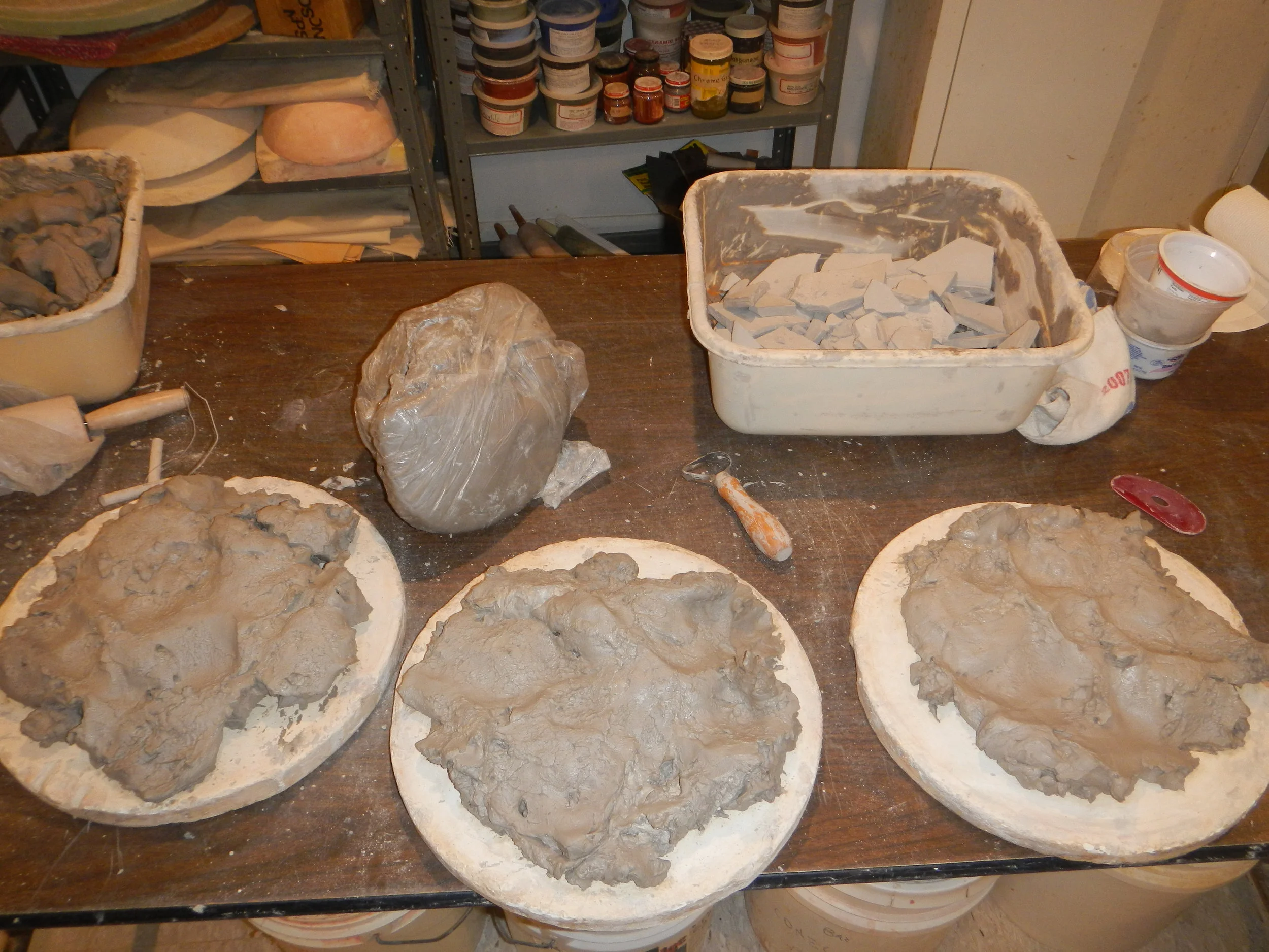 Slaked clay firming up a bit on plaster, nearly ready to wedge. More slaked clay in basins, not seen in the picture, to be spread on batts after this batch and the next batch and... (And more dry clay scrap already building up, in the background.)