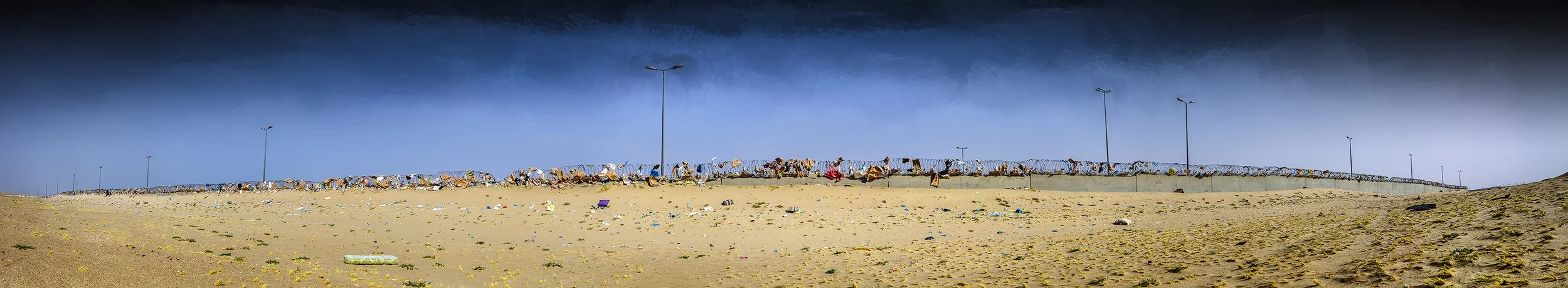 The Wall . (2016) Crowned concrete wall with barbed wire, being swallowed by the live desert as it traps wind blown rubbish.