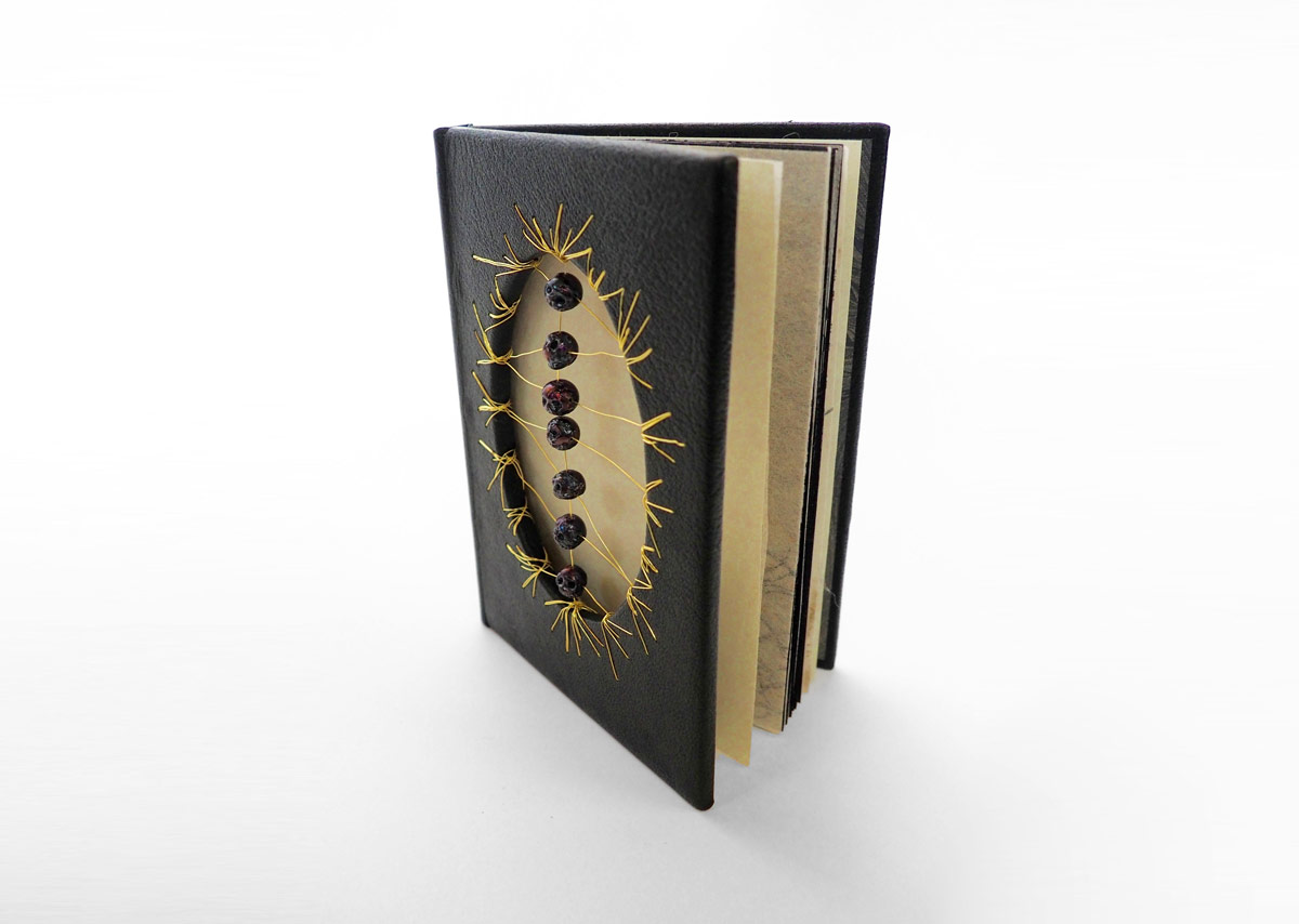   Materials:  Full leather binding with a hollow tube. Covered in green goat skin leather with hand sewn silk endbands. Gold metal wiring interlaced into the front cover to hold the 7 hand carved black pearl skulls. Hand marbled pastedowns and Japane