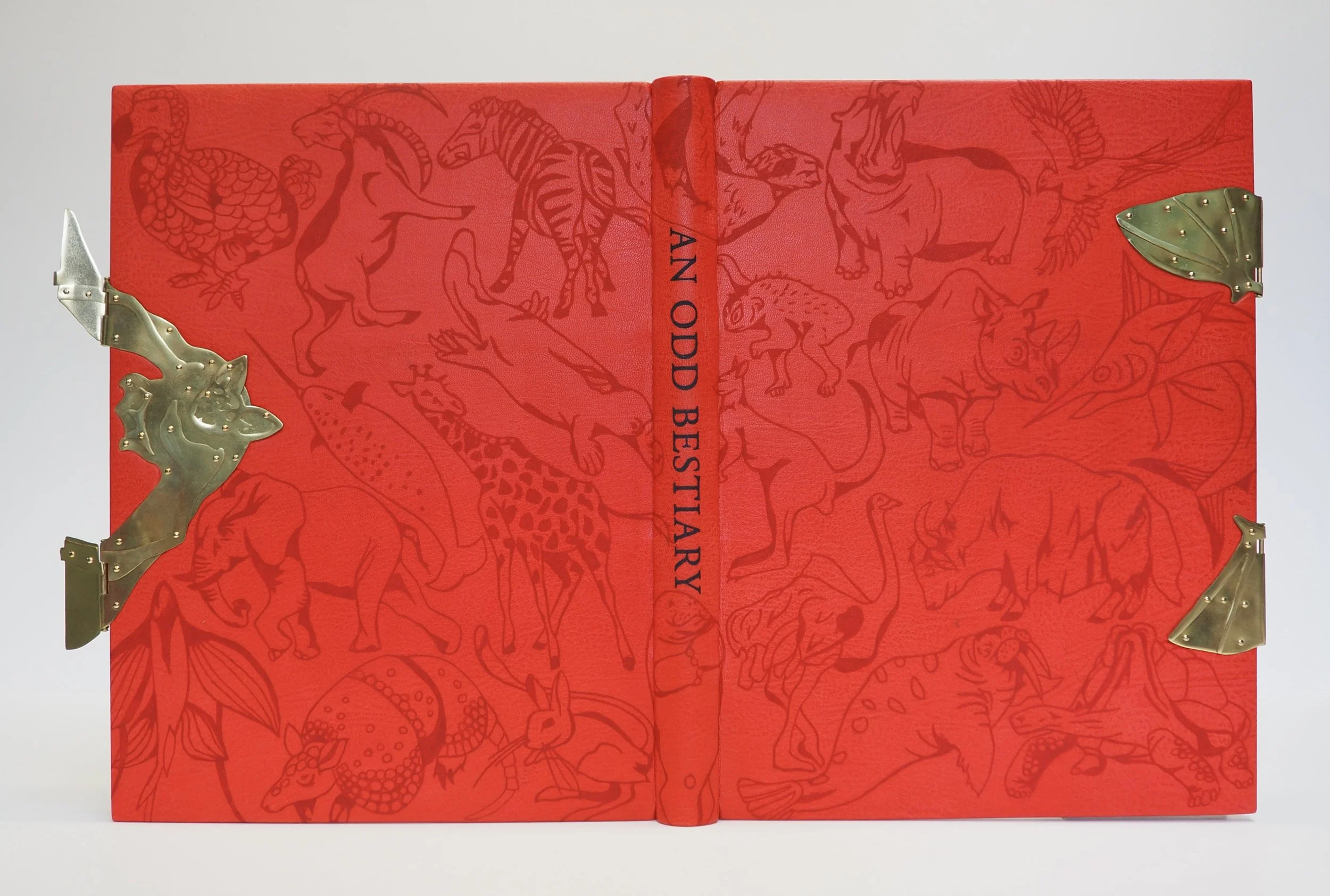  An Odd Bestiary by Cheloniidae Press  10.6” w x 13.6” h x 1.2” d  Materials: red goat skin, brass, tattoo ink, paste paper, book cloth.  Book bound in red goat skin, with black and red tattoo designs and a hand cut out brass bat fore-edge clasp. Tig