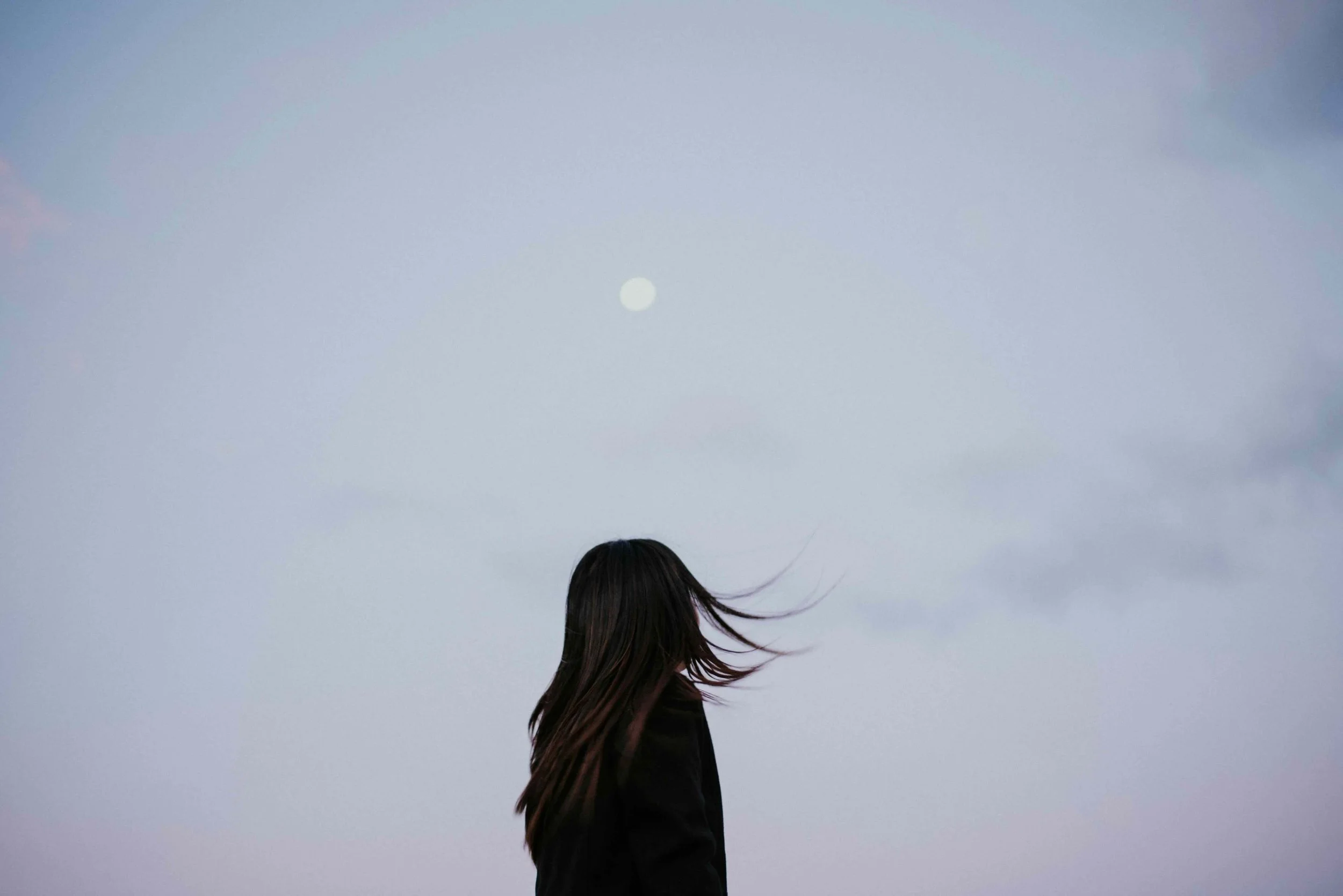 Woman with long dark hair blowing in the wind beneath a full moon at dusk, evoking change during perimenopause