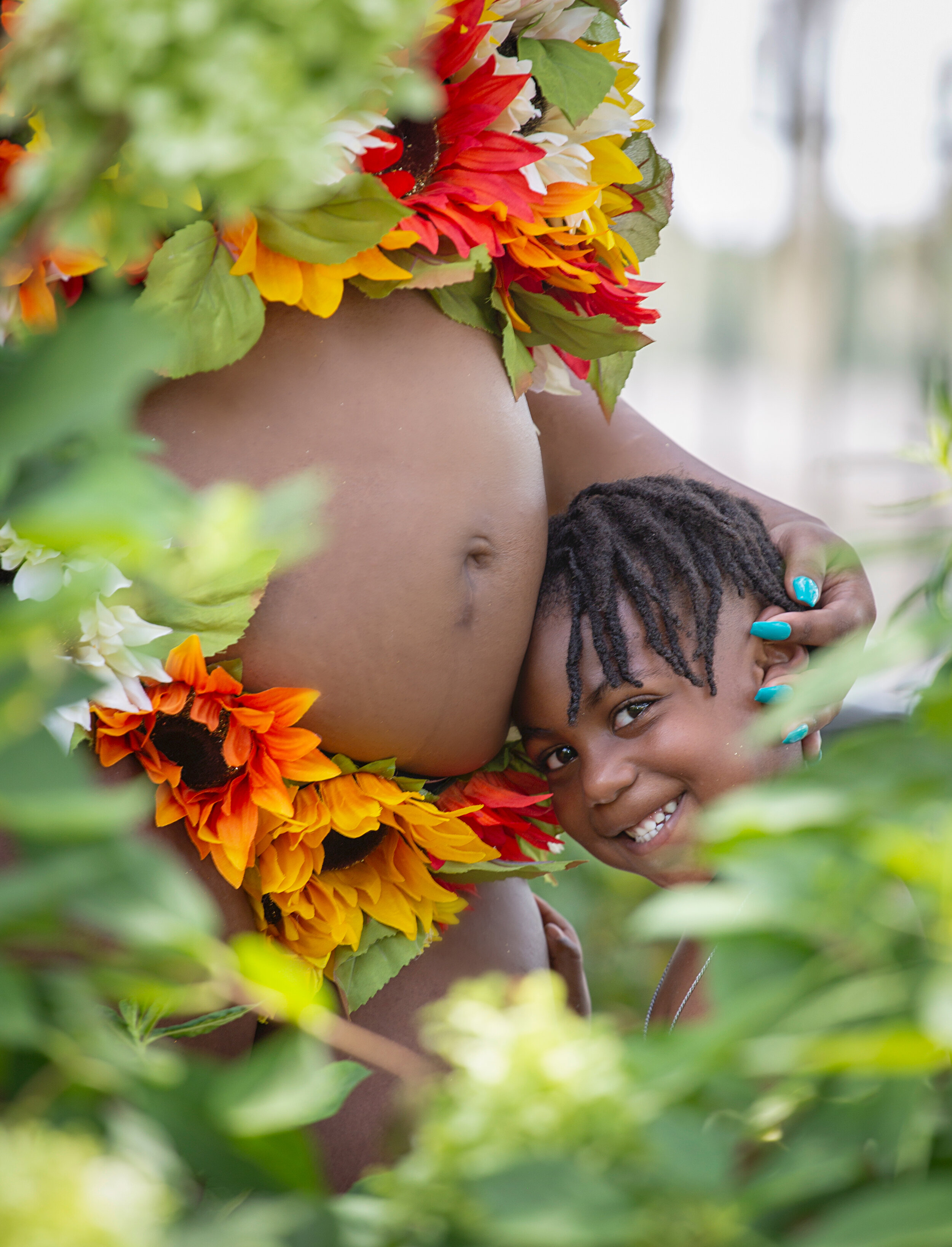 A joyful peek-a-boo moment with a soon-to-be big brother, his smile framed by vibrant sunflowers, at the New Orleans Botanical Garden