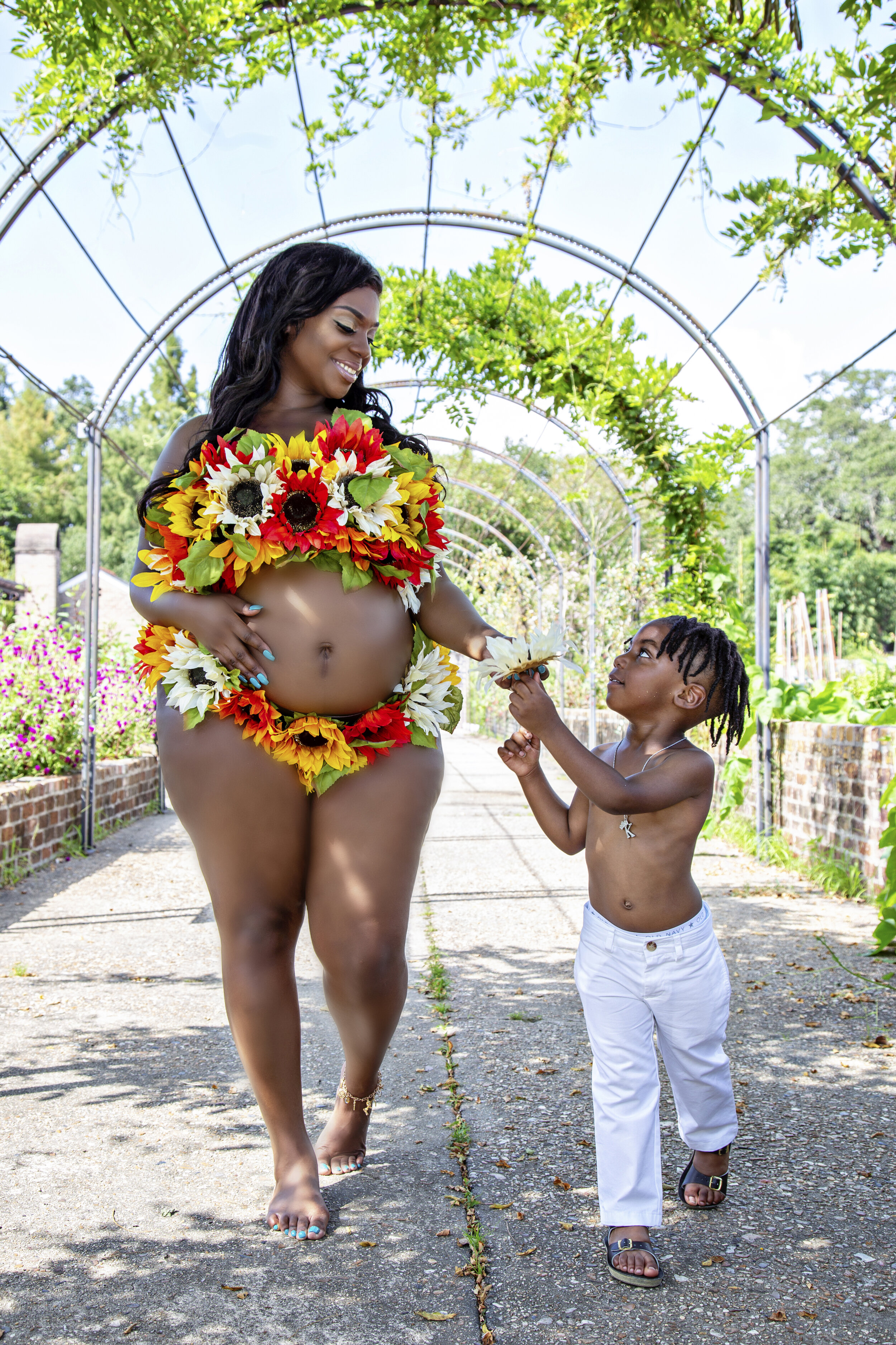 Expectant mother Britt adorned with a sunflower ensemble, sharing a natural moment with her son at New Orleans Botanical Garden