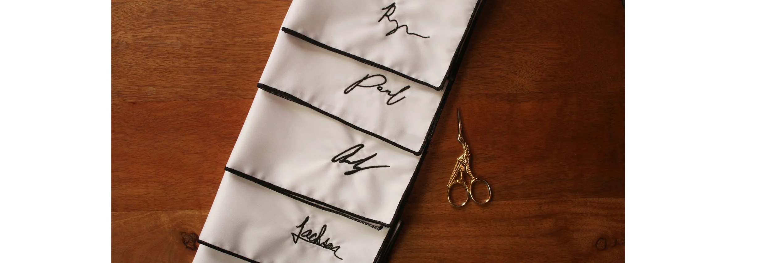 Organization of cloth swatches labeled with names, placed on a wooden surface with a pair of gold scissors nearby.