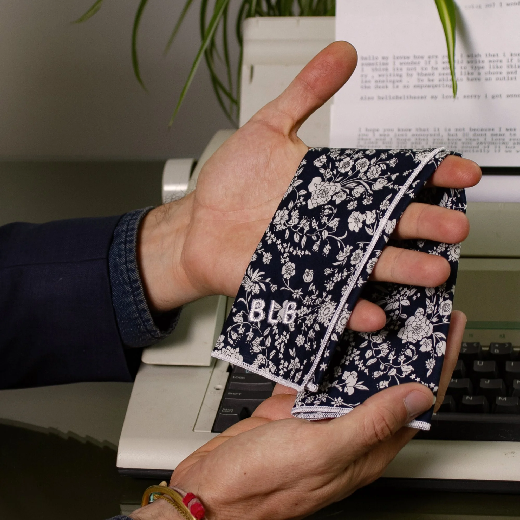 Person holding a navy blue floral pocket square with a monogram 