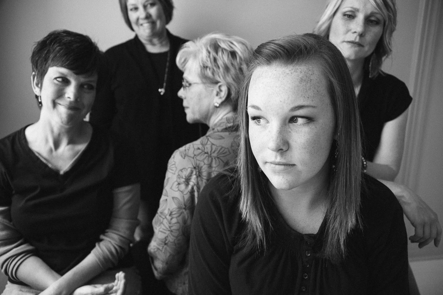 Black and white photo of five women, with one young woman in the foreground looking to the side and four older women behind her, some looking at the camera and some turned away.