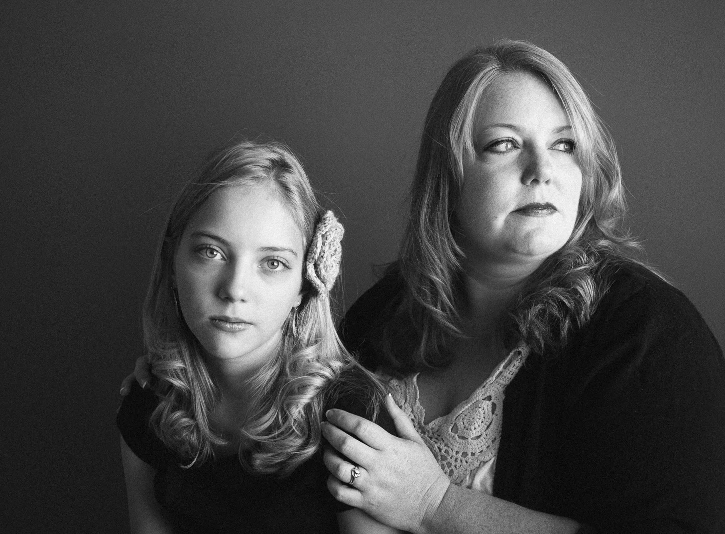 Black and white portrait of a woman and a girl, both with blonde hair, looking away from the camera, with the woman resting her hand on the girl's shoulder.