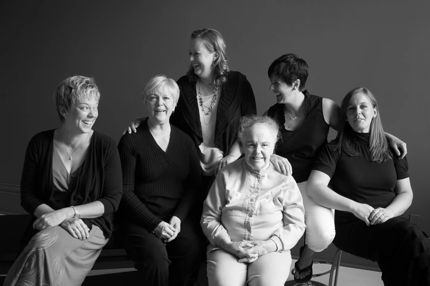 Black and white photo of seven women of different ages sitting and standing together, smiling and laughing.