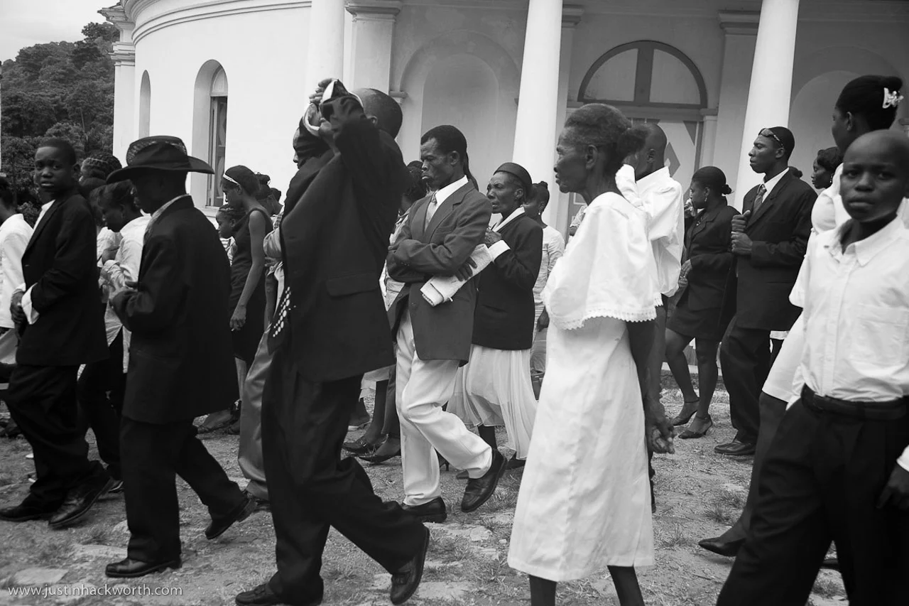A group of people dressed in formal clothing, walking in front of a church building, participating in an outdoor event or ceremony.