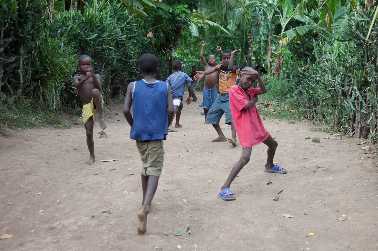 A group of children playing on a dirt path surrounded by lush green tropical plants and cacti.