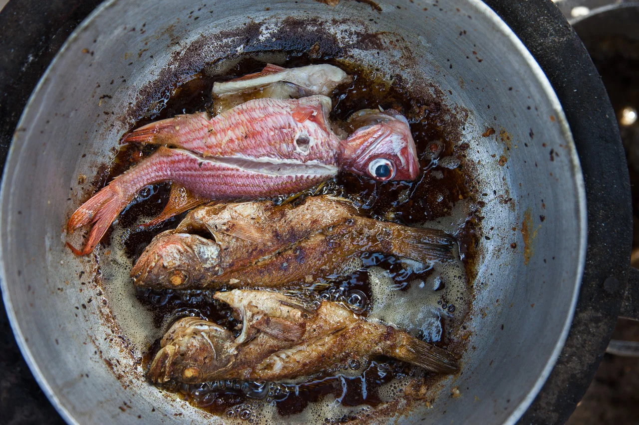 Multiple fish being cooked in a pan with bubbling oil.