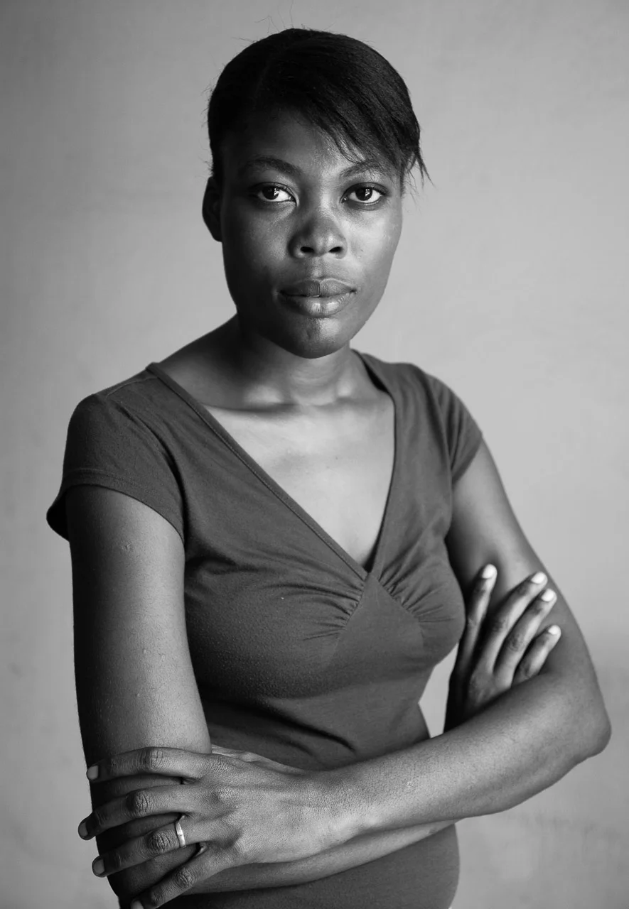 Black and white portrait of a woman with crossed arms looking directly at the camera, short hair, plain background.