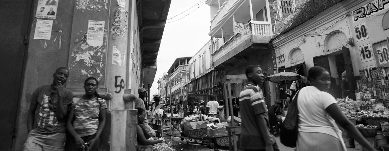 Street scene in Haiti with pedestrians and market stalls in an urban area, black and white photo.